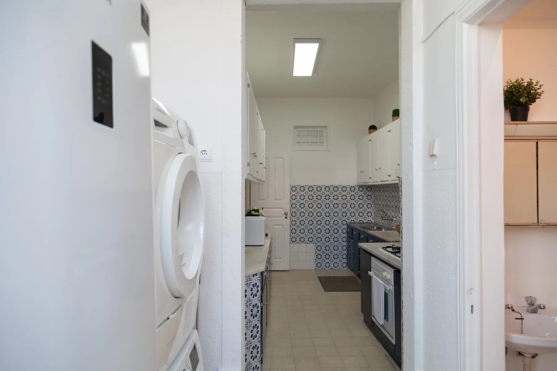 Una cocina estrecha con salpicadero de azulejos estampados y armarios blancos.