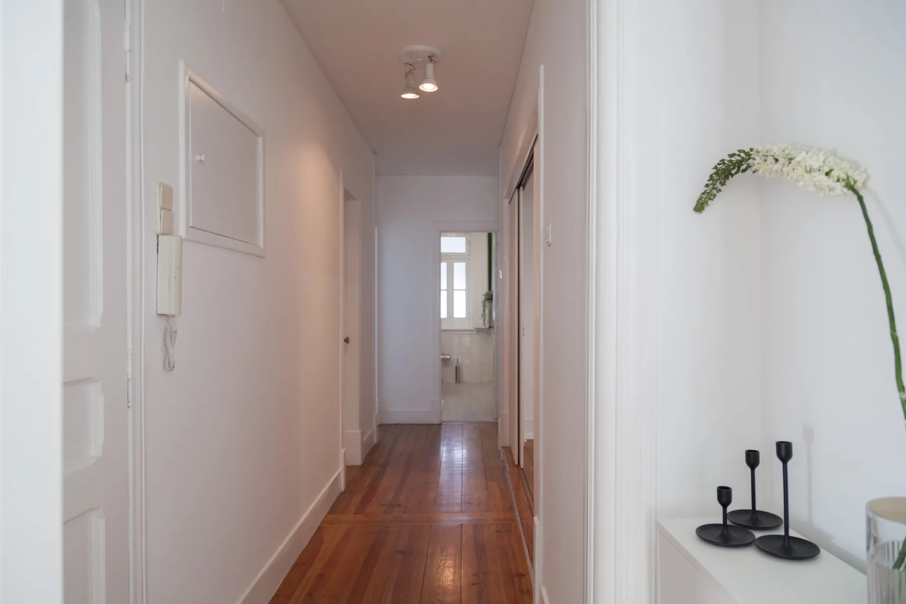 Un pasillo estrecho con suelo de madera pulida conduce a una habitación luminosa.