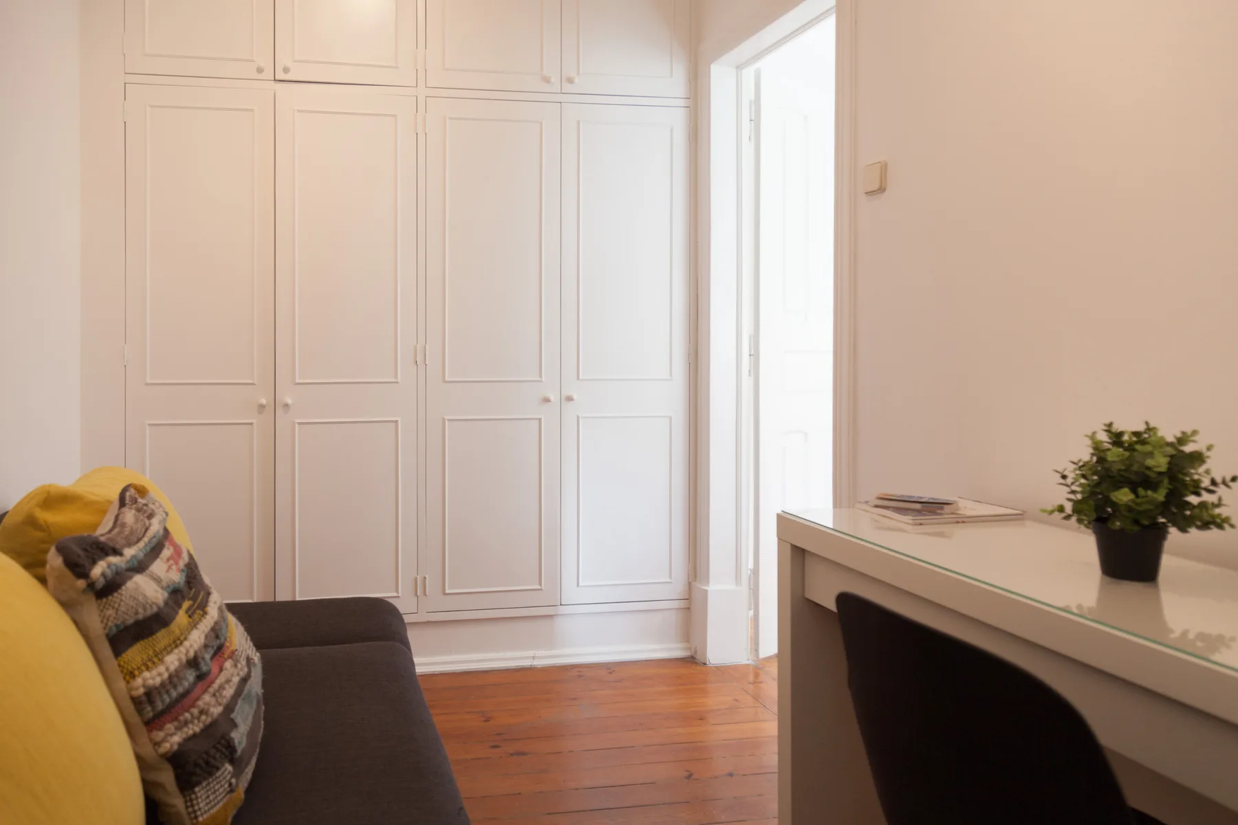Zona de estar de un dormitorio con un sofá junto a armarios empotrados y un escritorio.