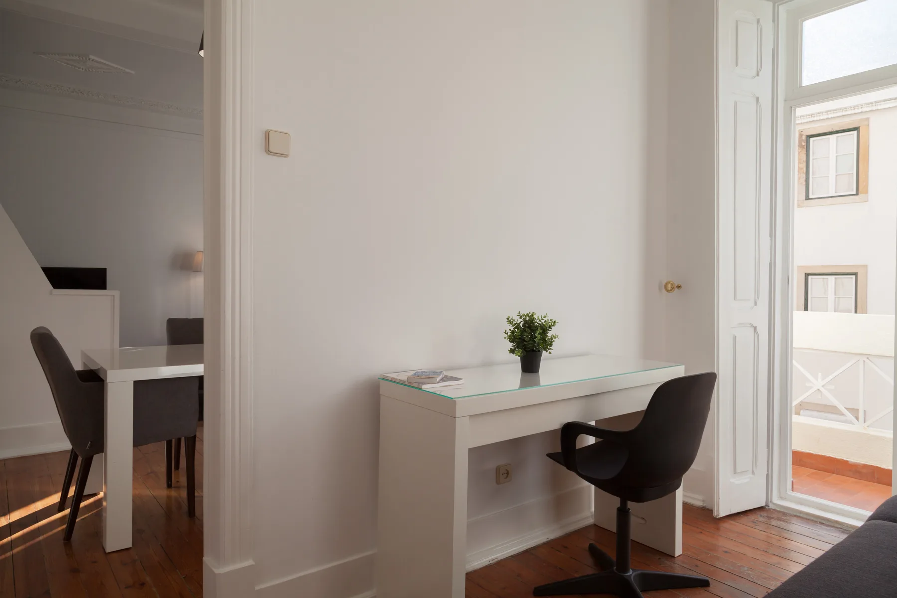 Una habitación luminosa con un escritorio y una silla junto a una ventana alta.