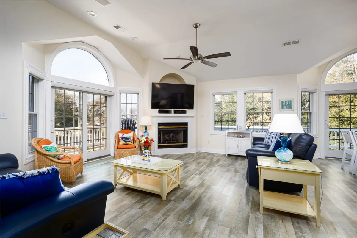 A bright living room with seating, large windows, and a fireplace.