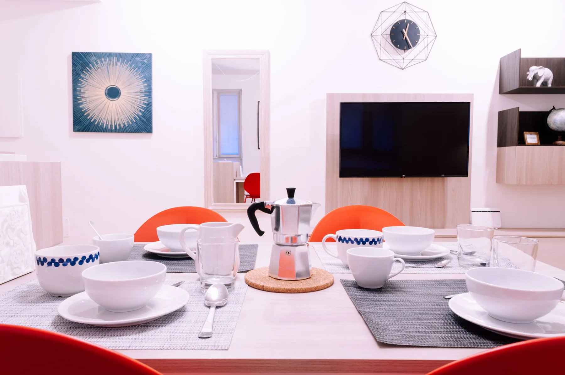 Una mesa de comedor está puesta con vajilla frente a un televisor montado en la pared.