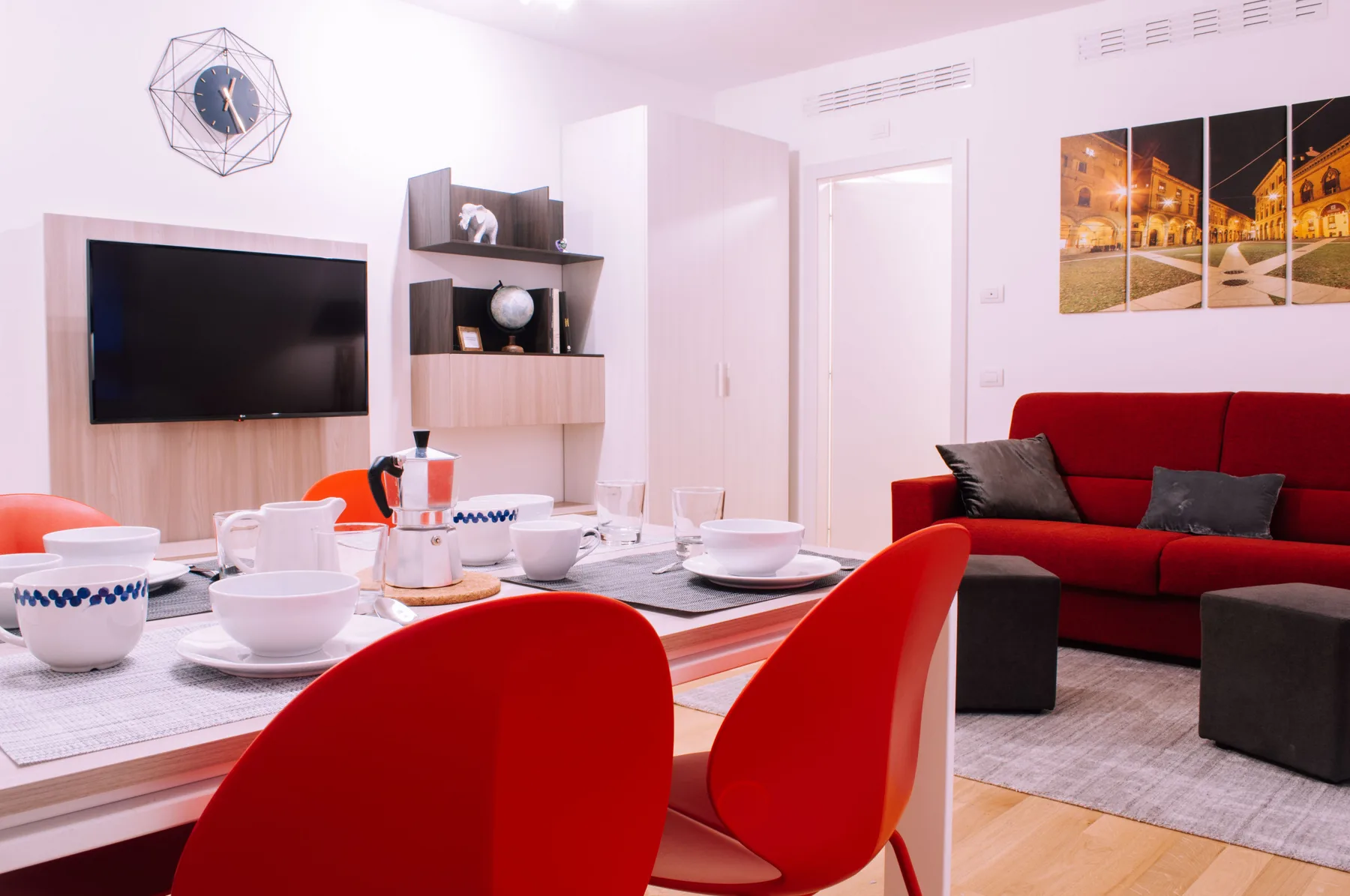 Una luminosa sala de estar y comedor con la mesa puesta, asientos rojos y un televisor en la pared.