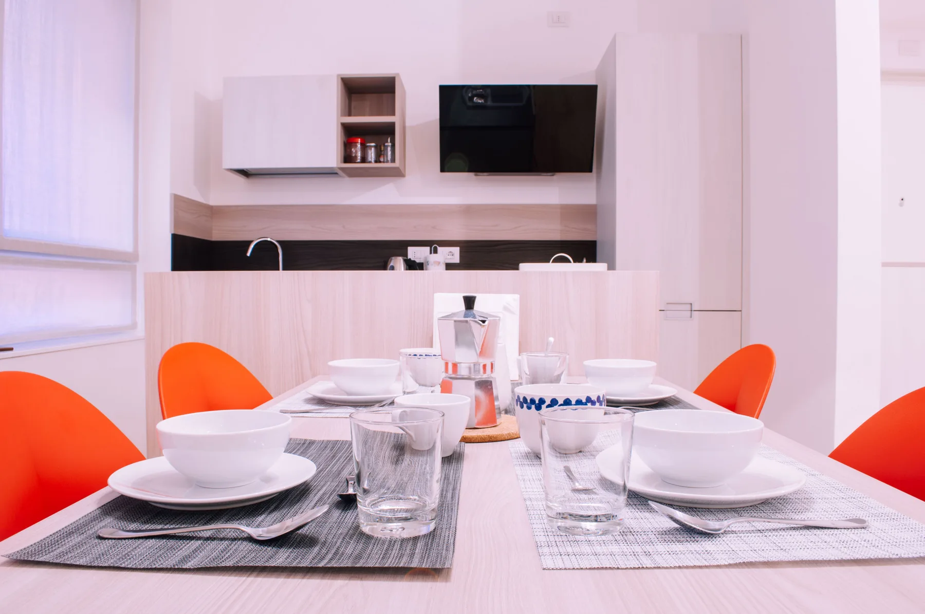 Una mesa de comedor está puesta con platos frente a una cocina compacta.