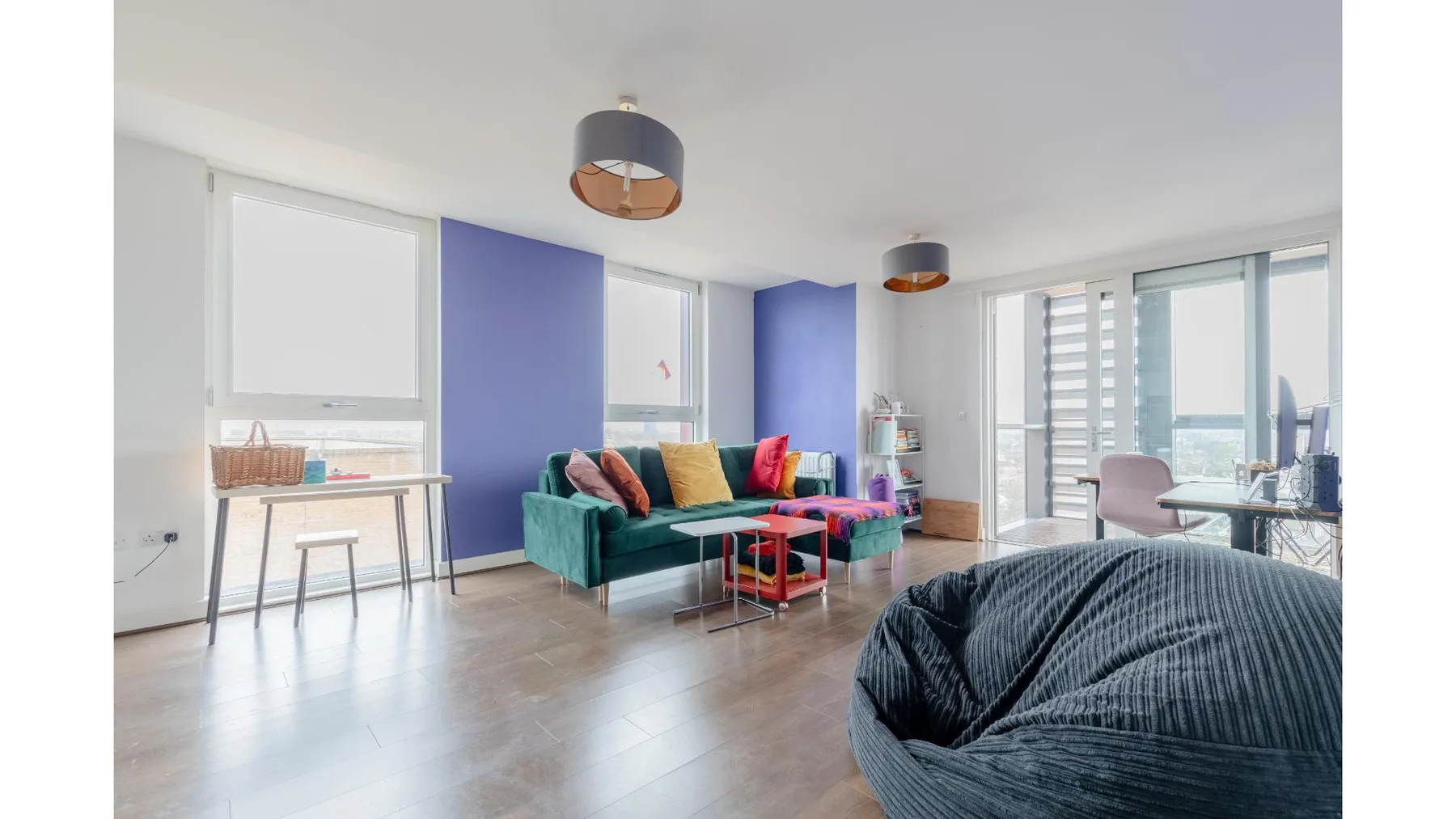 A bright living area with colorful seating beside large windows.
