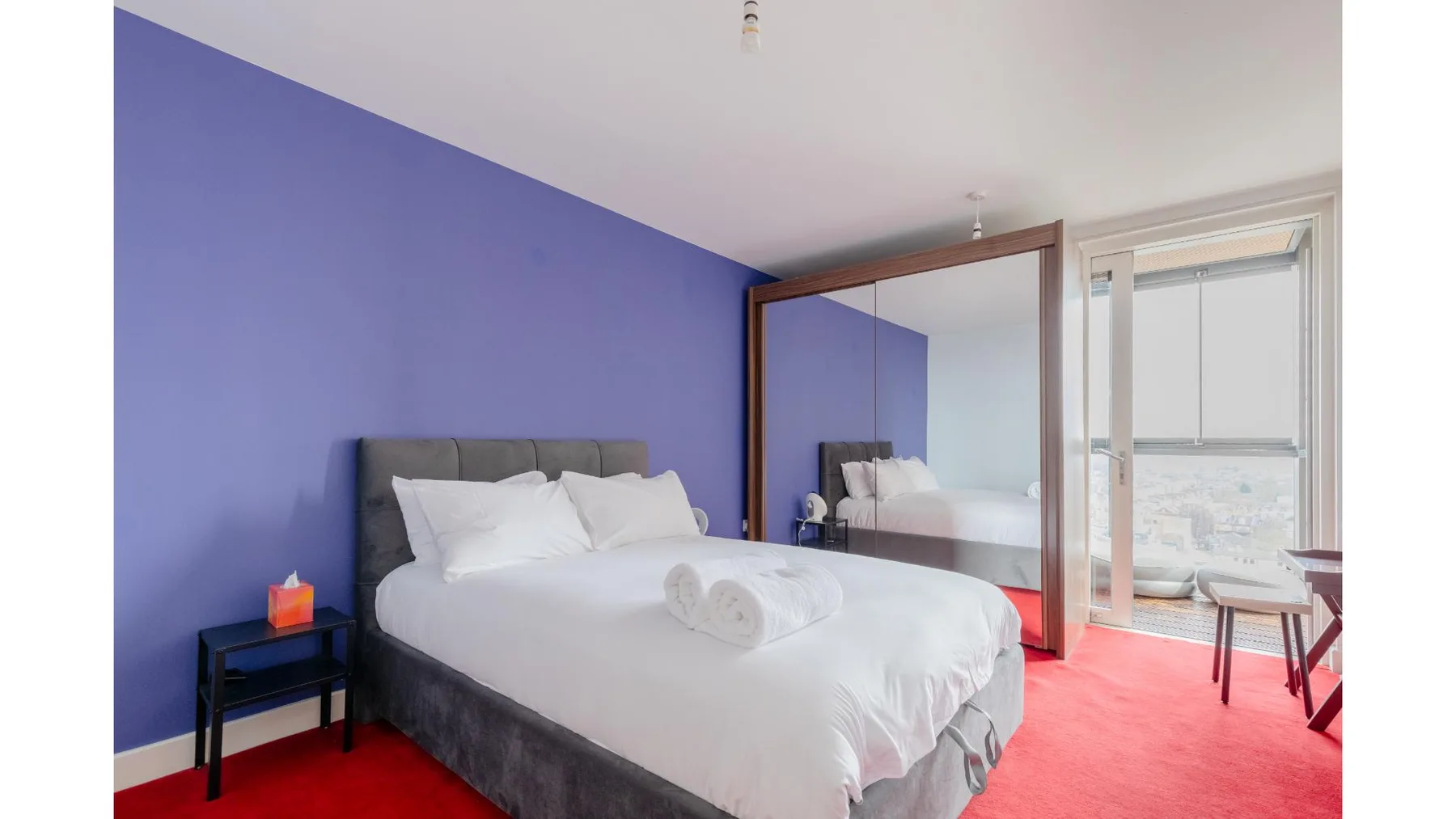 A bedroom with a white bed, blue wall, and mirrored wardrobe.