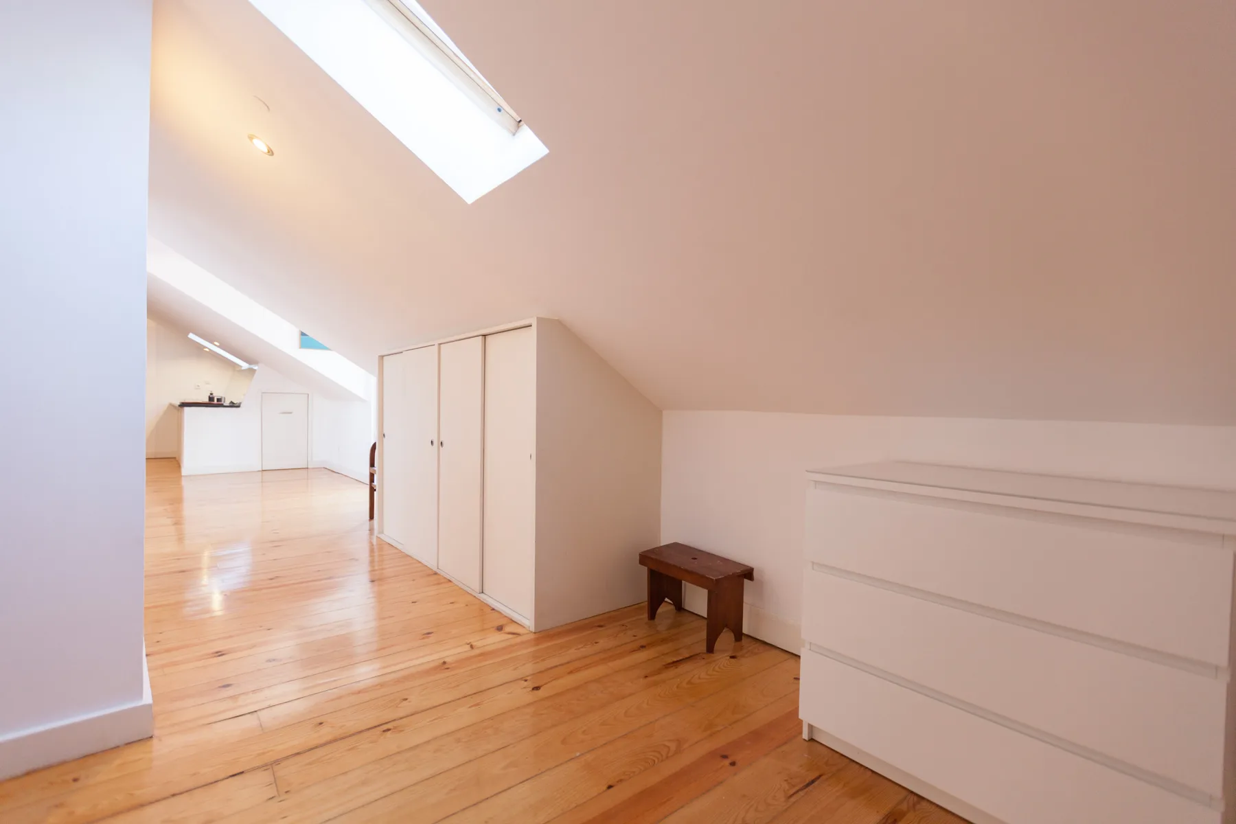 Una luminosa habitación abuhardillada con techo inclinado, tragaluz y suelo de madera.