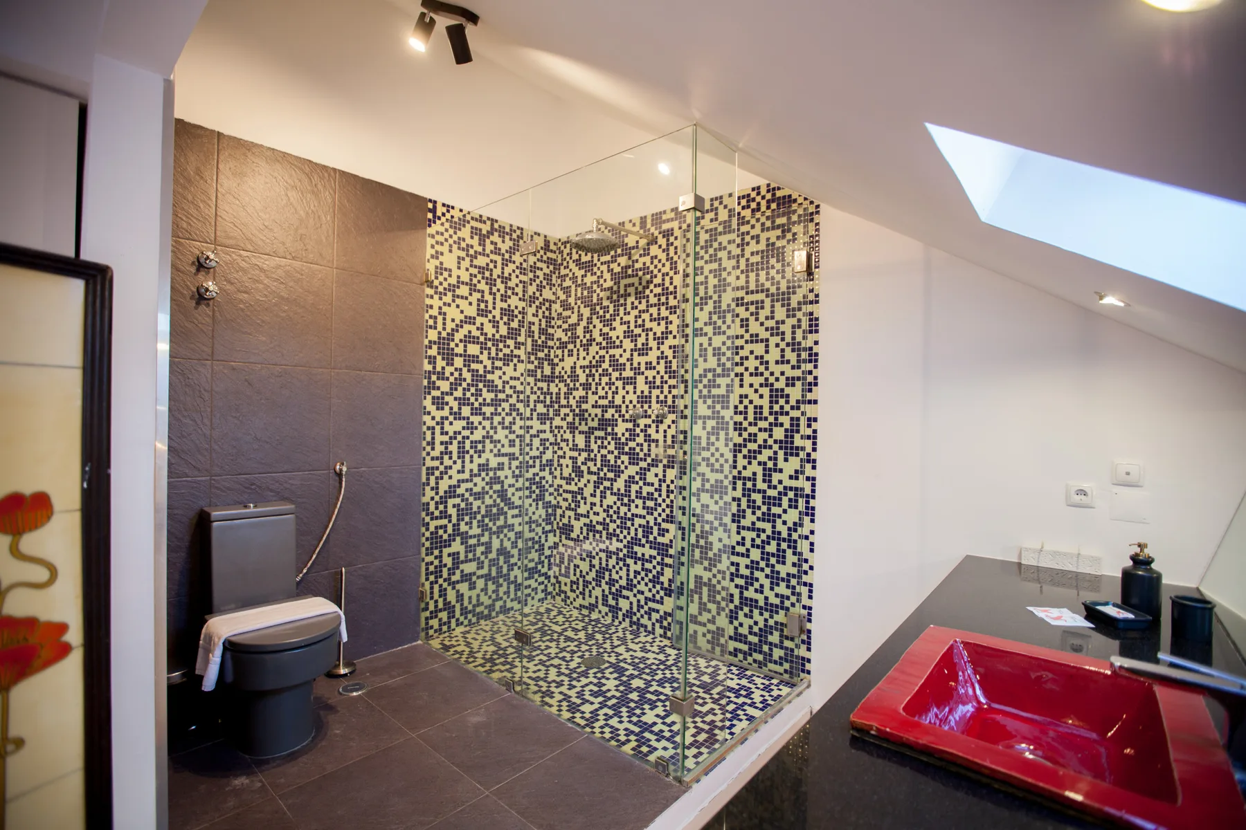 Un baño con ducha de vidrio, inodoro y lavabo rojo.