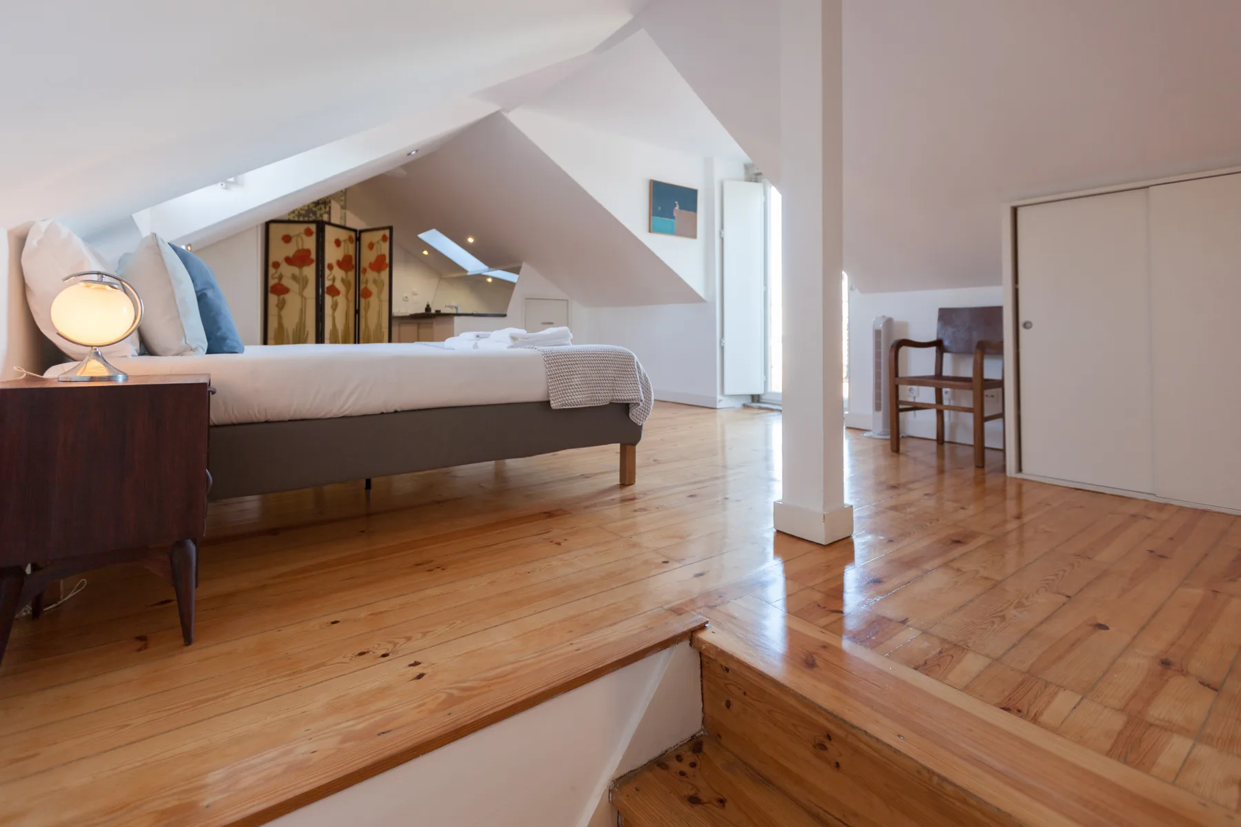 Dormitorio con una cama y suelo de madera bajo un techo inclinado.