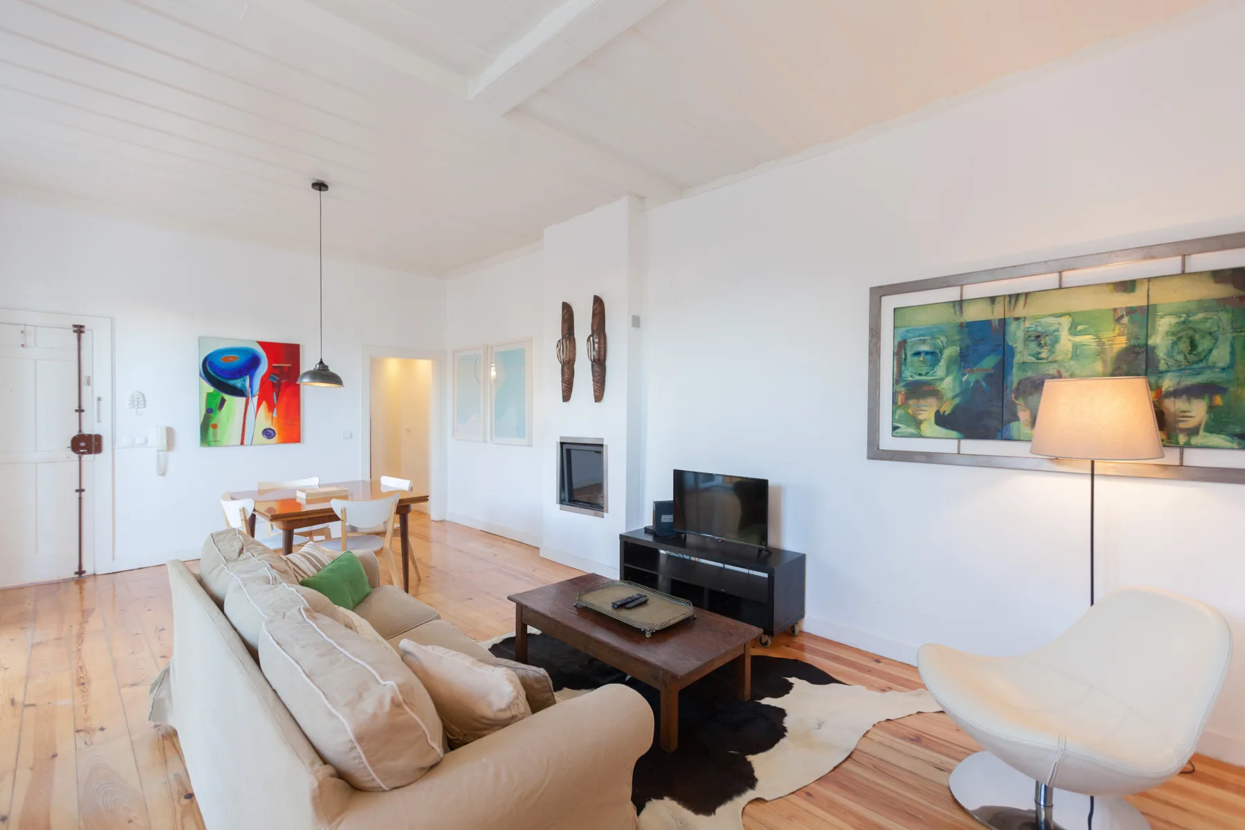 Una sala de estar luminosa con asientos, un televisor y arte colorido en las paredes.