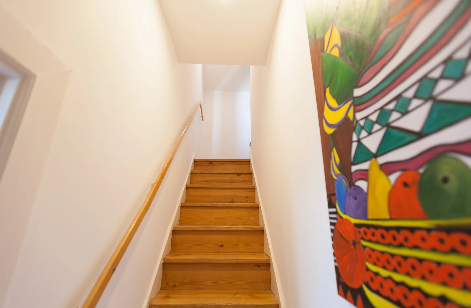 Una escalera estrecha con peldaños de madera y un tapiz colorido estampado.