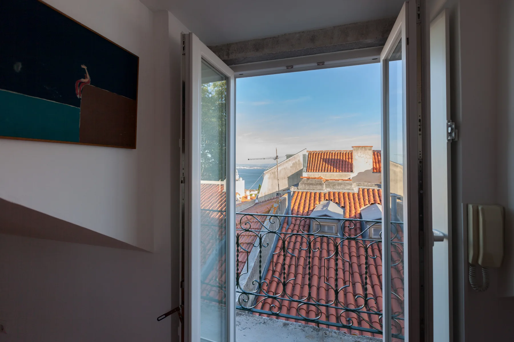 Una ventana abierta da a tejados de terracota y una zona costera a lo lejos.