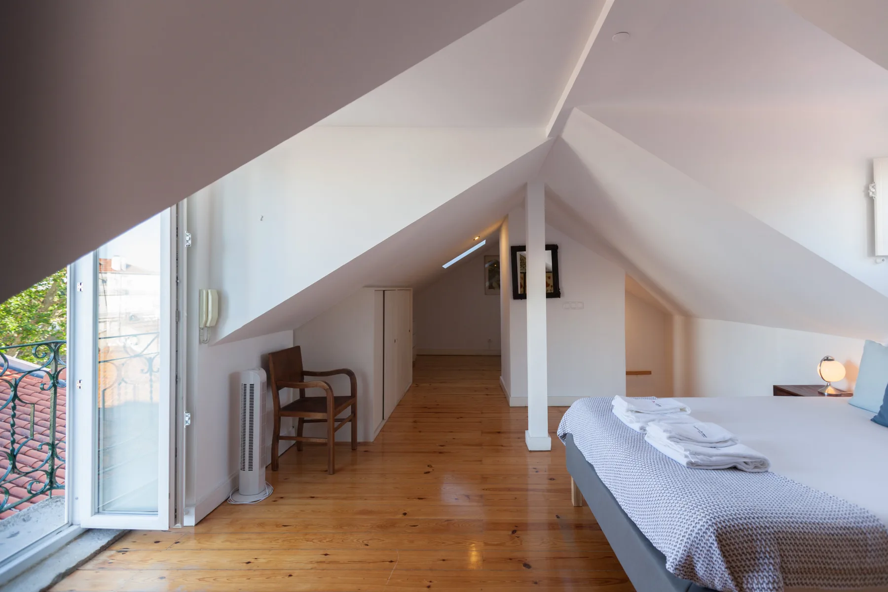 Un dormitorio abuhardillado luminoso con una cama, suelo de madera y una puerta al balcón.