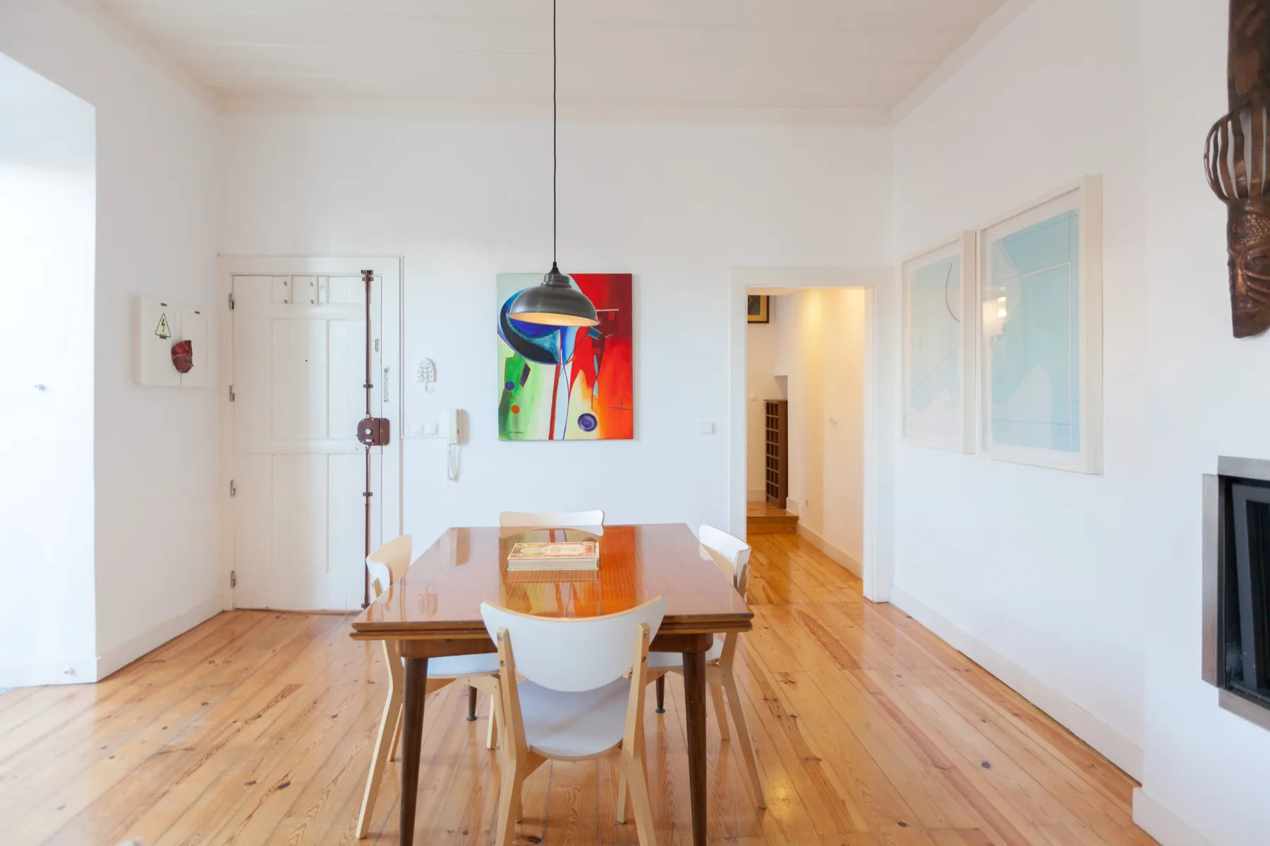 Un comedor luminoso con una mesa de madera bajo una lámpara colgante colorida.