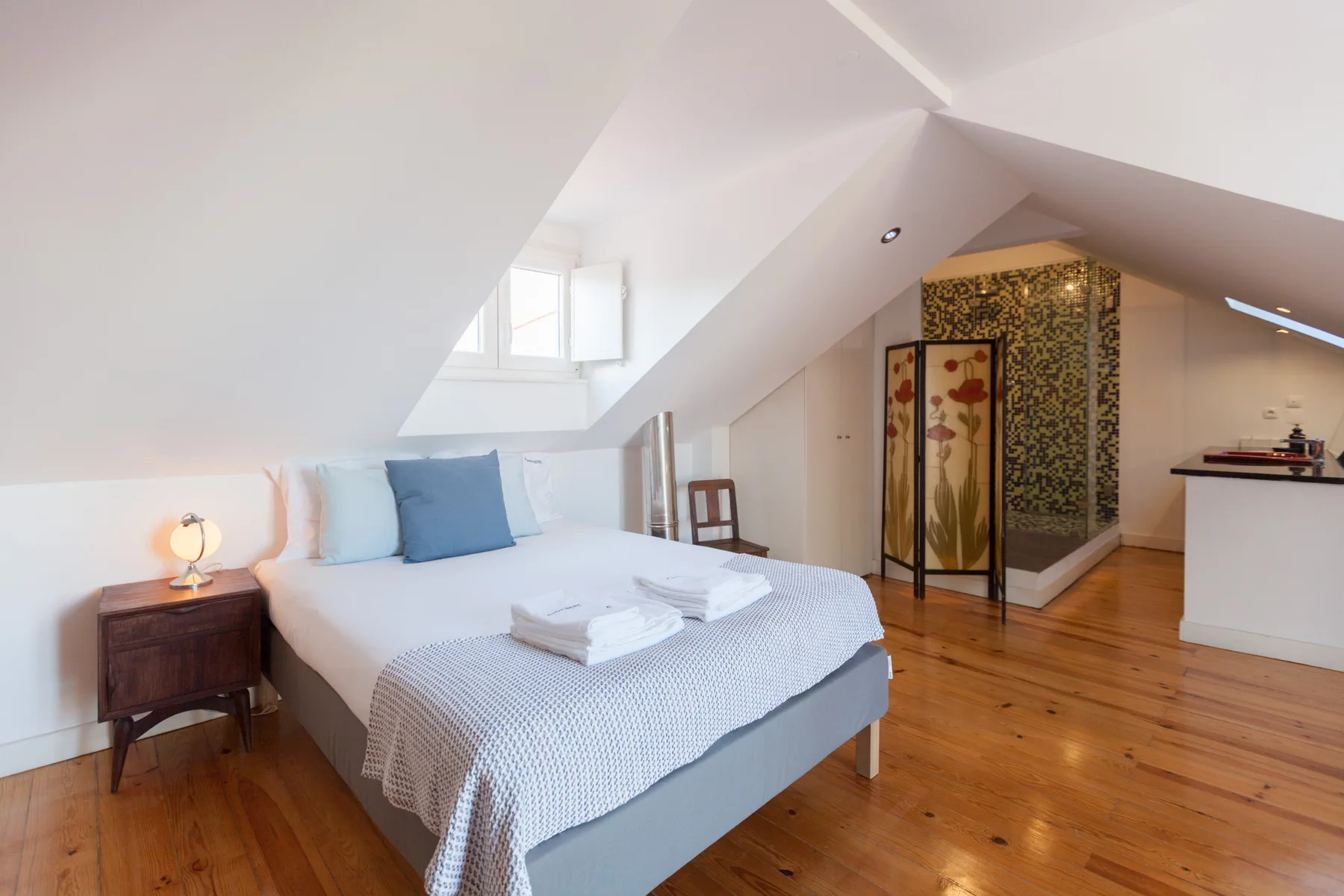 Un dormitorio con cama, mesita de noche y techo inclinado.