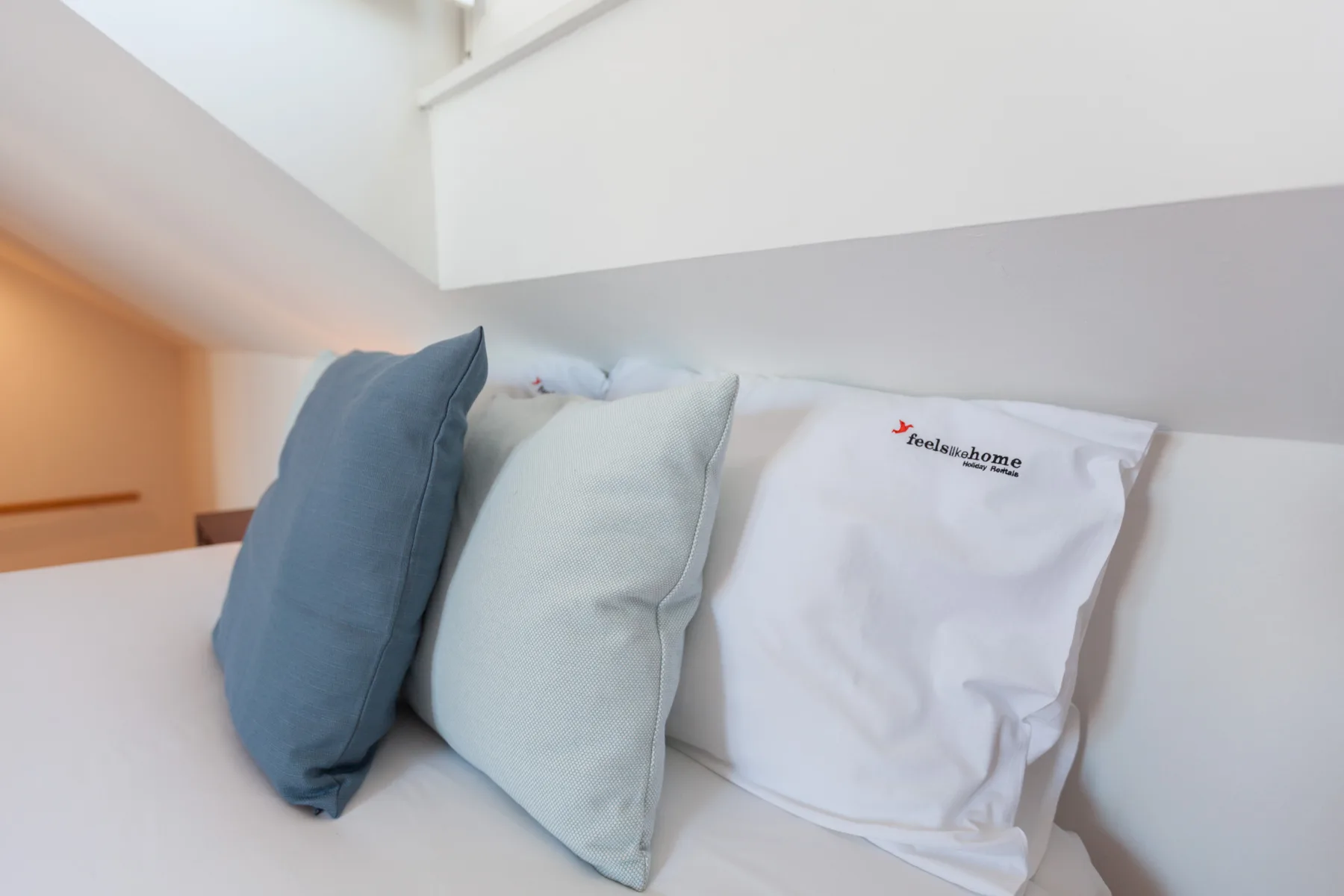 Una cama con almohadas azules y blancas bajo un techo inclinado.