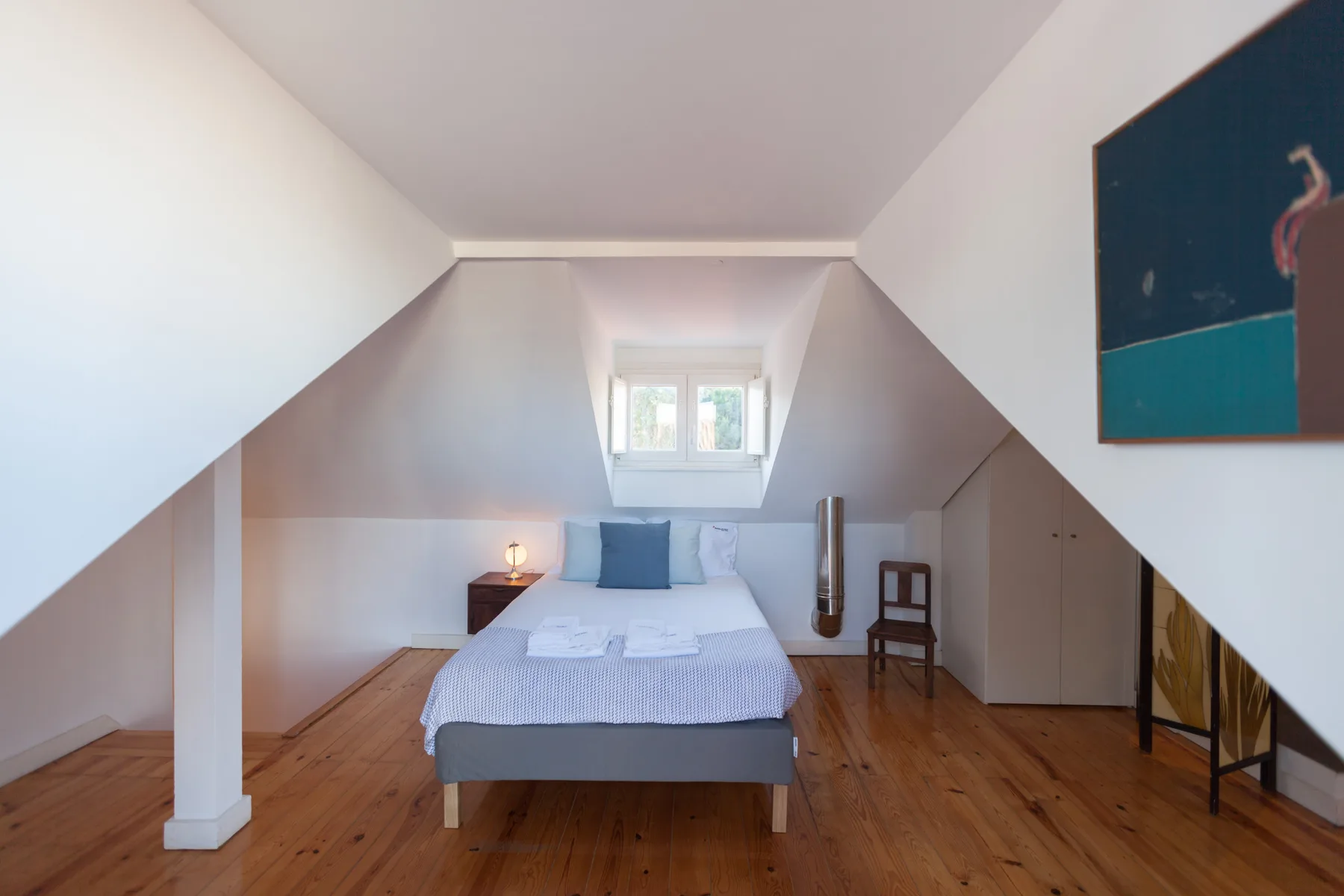 Un dormitorio con una cama bajo un techo inclinado y una ventana pequeña.