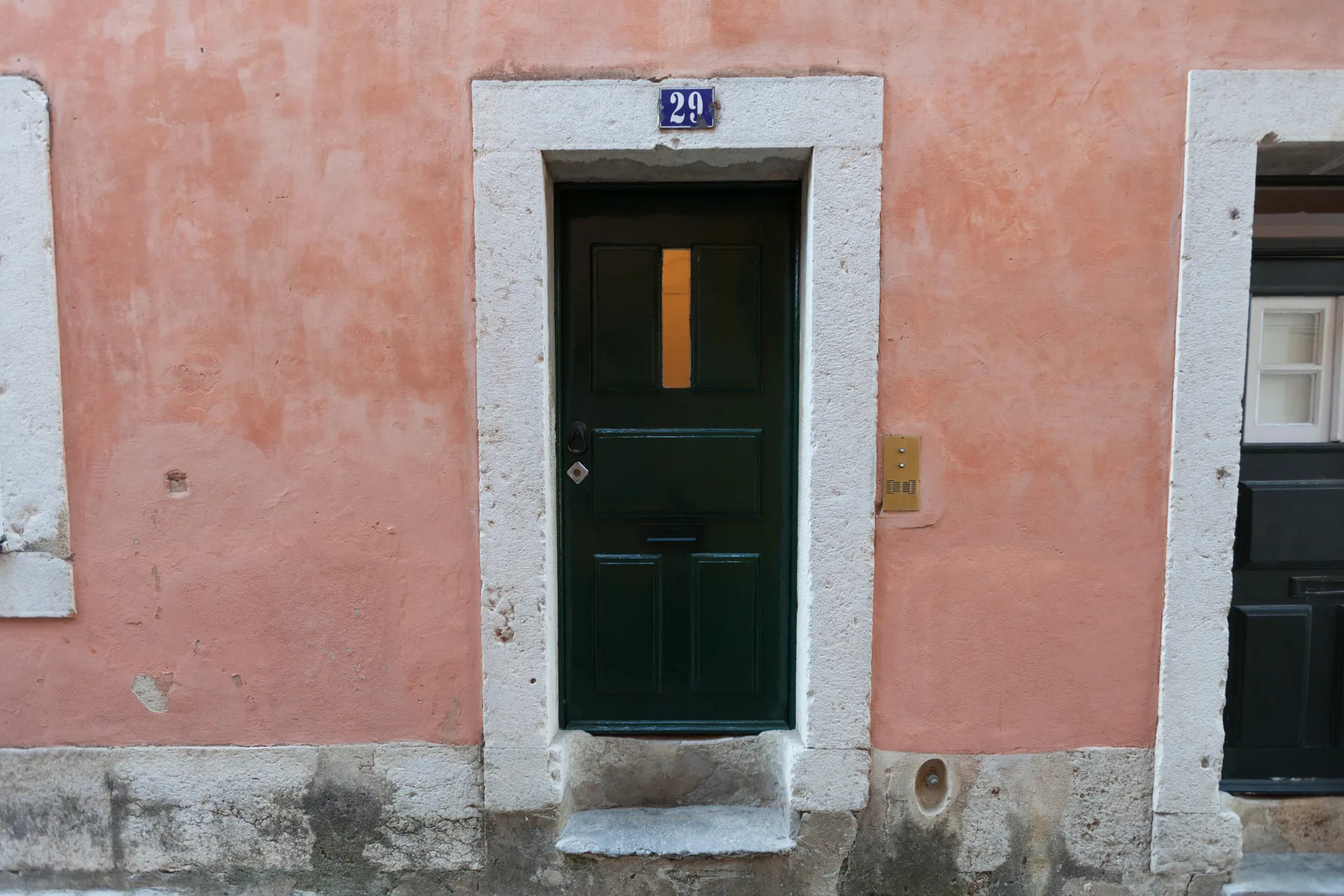 Una puerta de entrada verde oscuro en una fachada de estuco rosa.