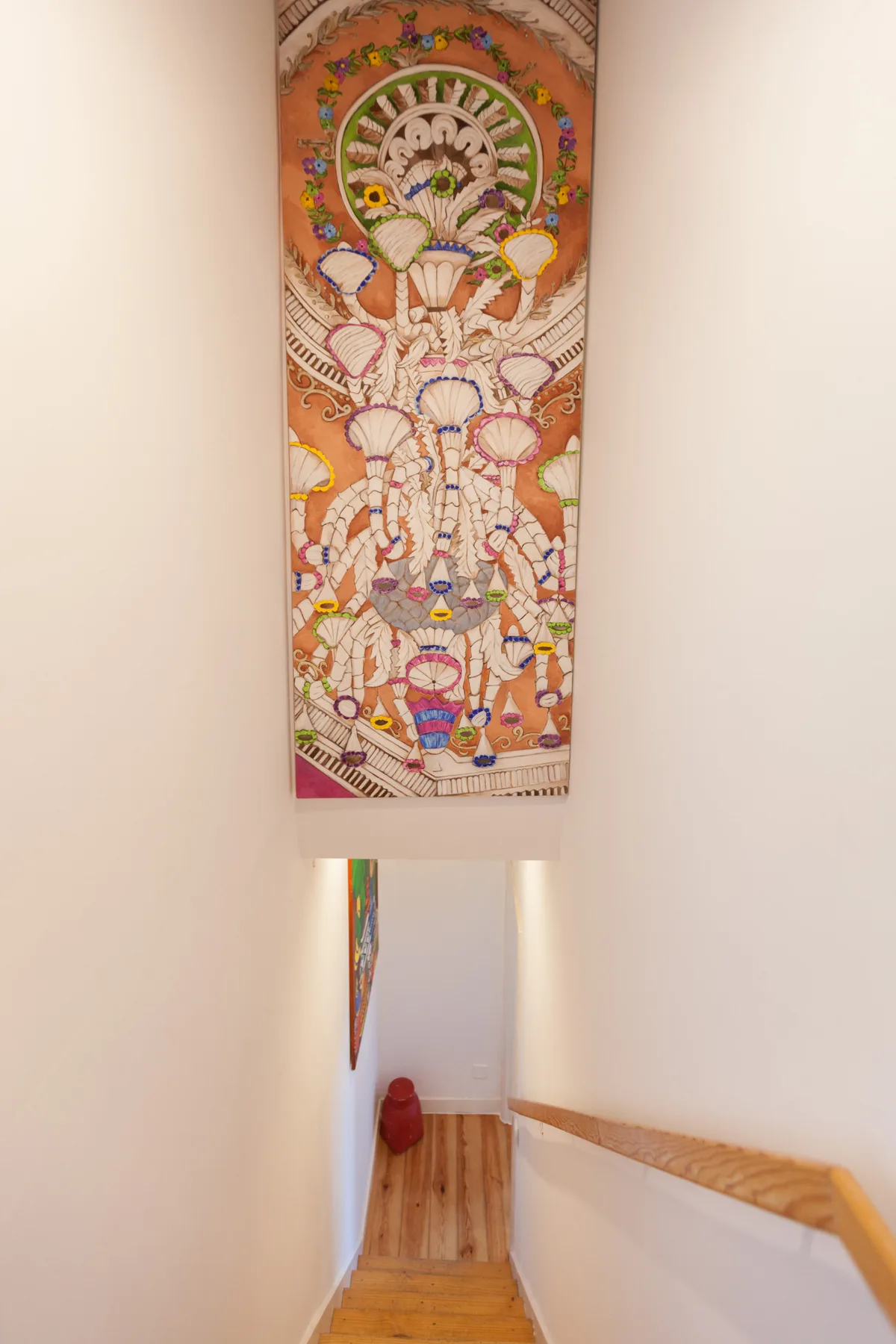 Una escalera estrecha con peldaños de madera y un tapiz decorativo colorido.