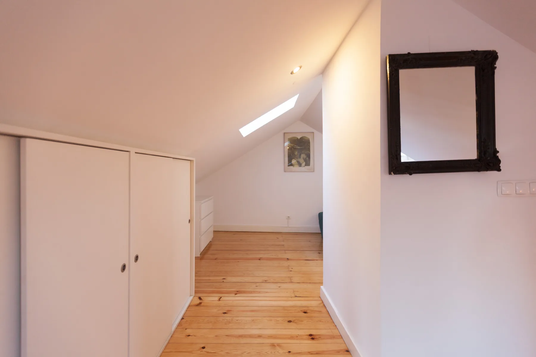 Una habitación con techo inclinado, armario empotrado y suelo de madera.