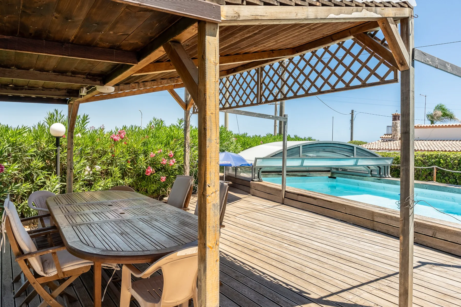 A wooden deck with shaded outdoor seating overlooks a swimming pool.