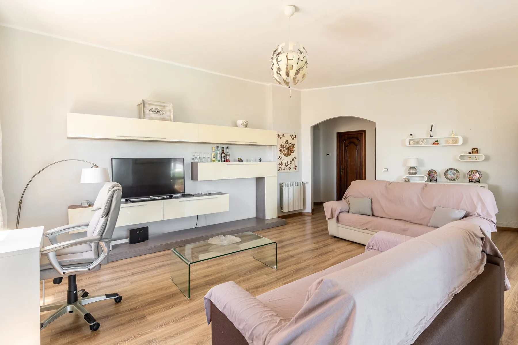 A bright living room with seating, a television, and a glass coffee table.