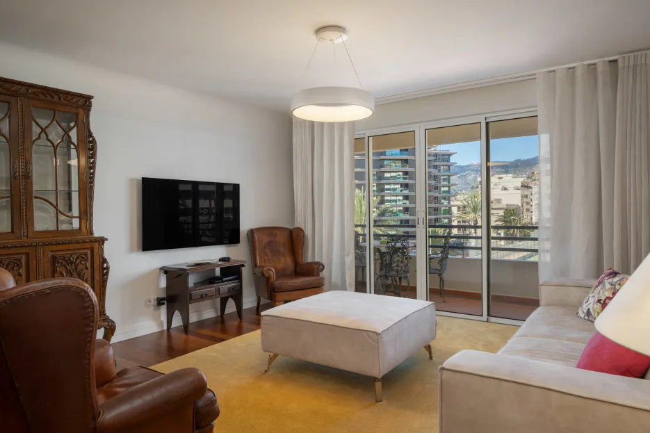 A living room with seating, a television, and glass doors opening onto a balcony.