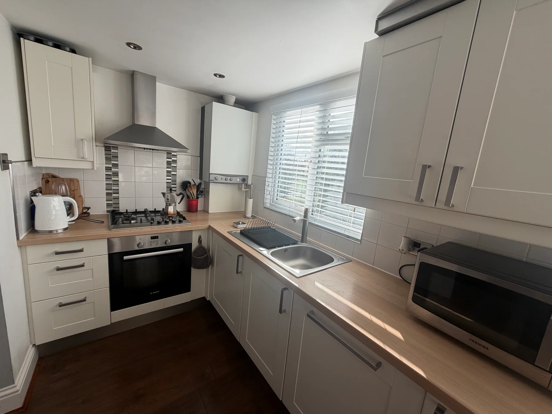 A bright kitchen with light cabinetry, a cooktop, and a sink beneath the window.