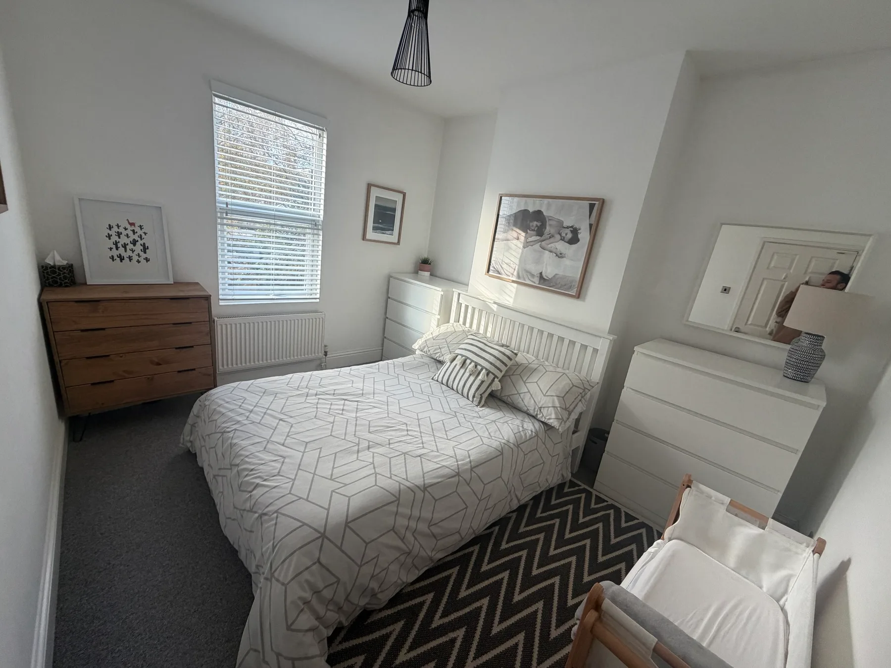 A bright bedroom with a patterned bed and a wooden dresser.