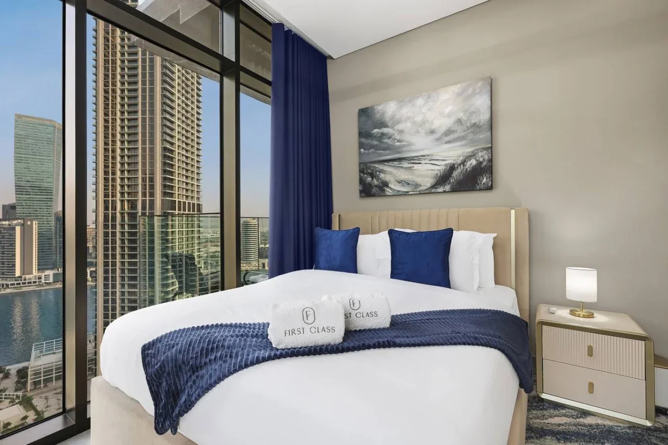 Un dormitorio con una cama blanca vestida con ropa de cama azul junto a grandes ventanas.