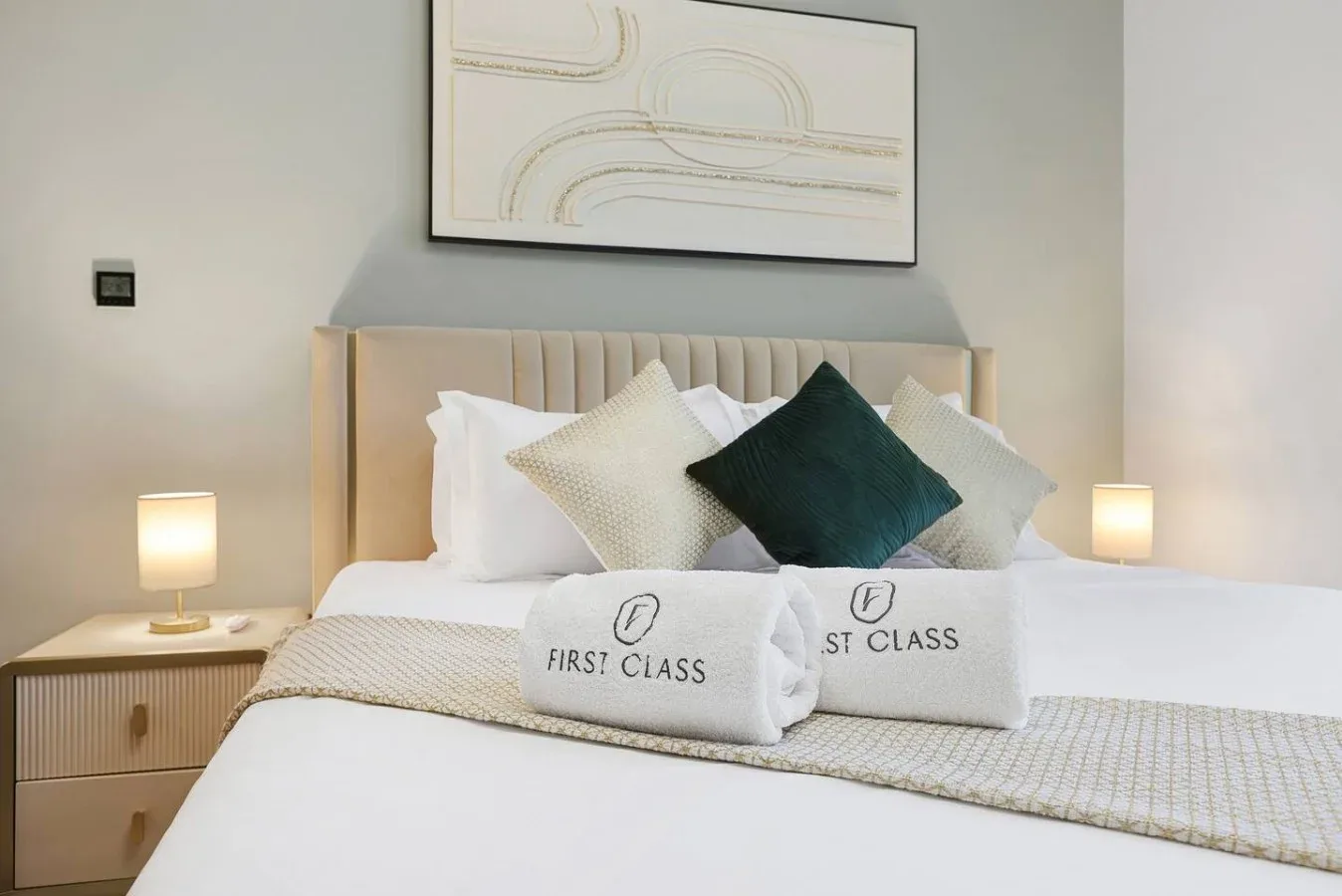 Una cama de dormitorio bien arreglada tiene almohadas superpuestas y toallas dobladas.