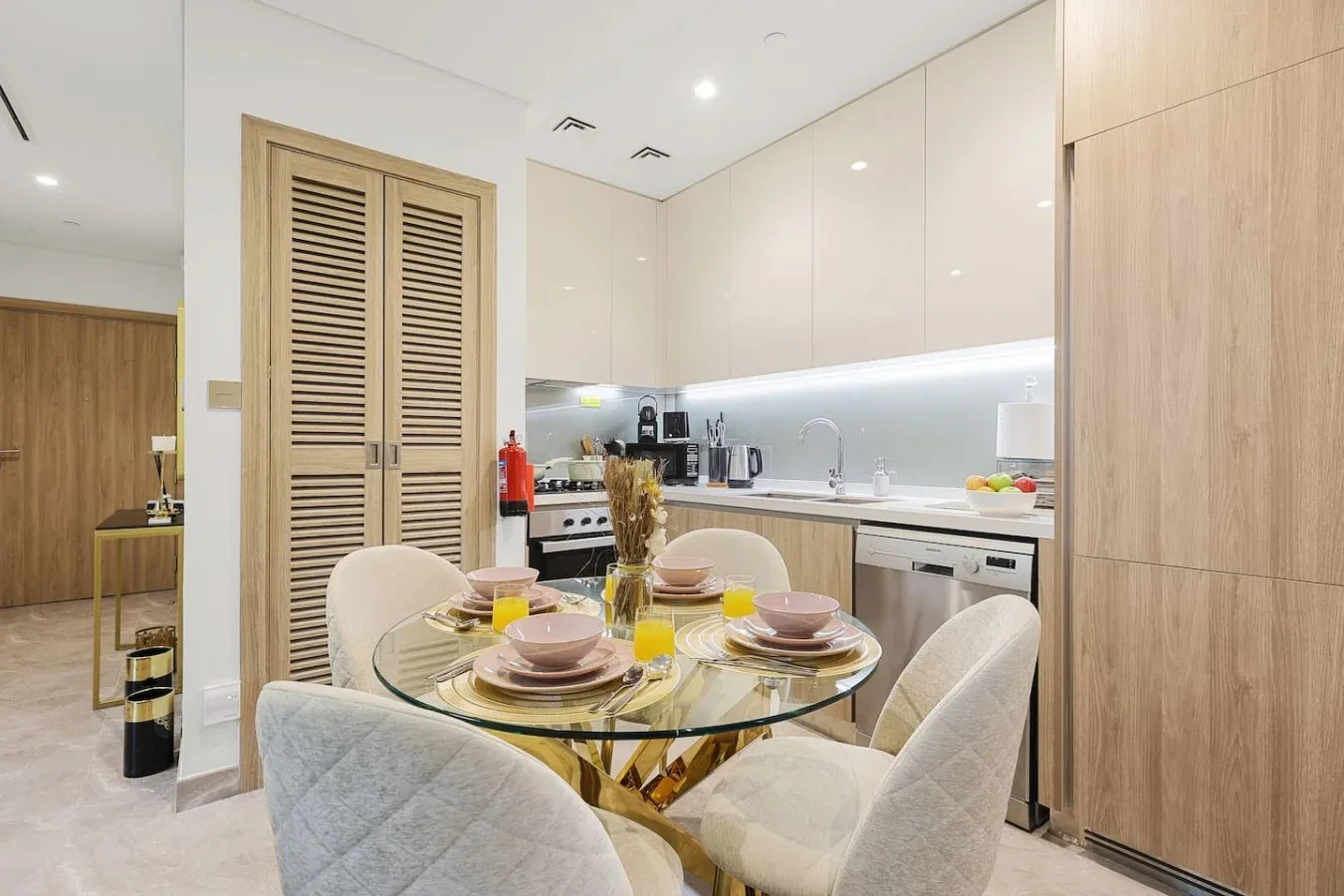 Una mesa de comedor puesta con vajilla está junto a una cocina moderna y luminosa.