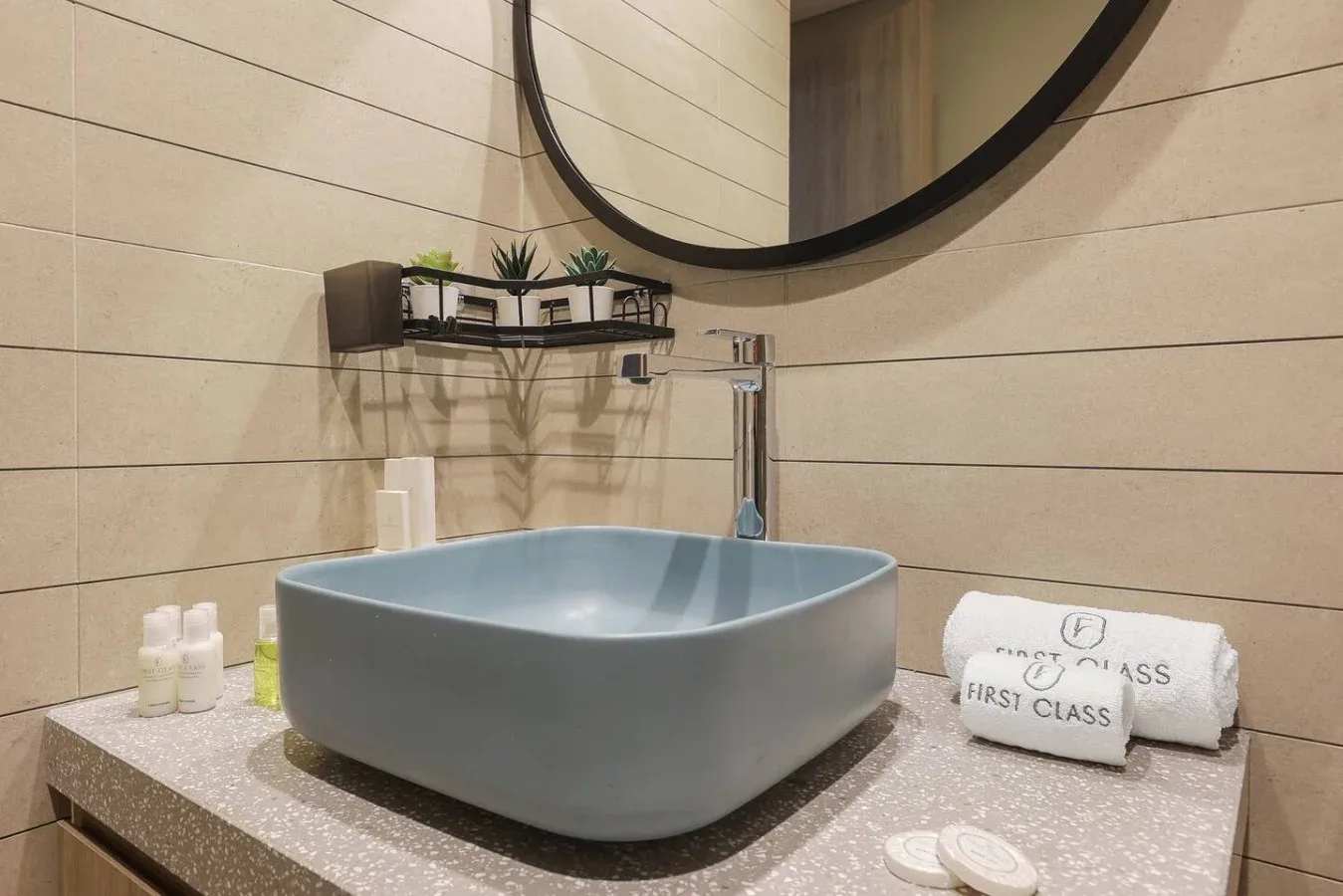 Un tocador de baño tiene un lavabo azul sobre encimera bajo un gran espejo redondo.