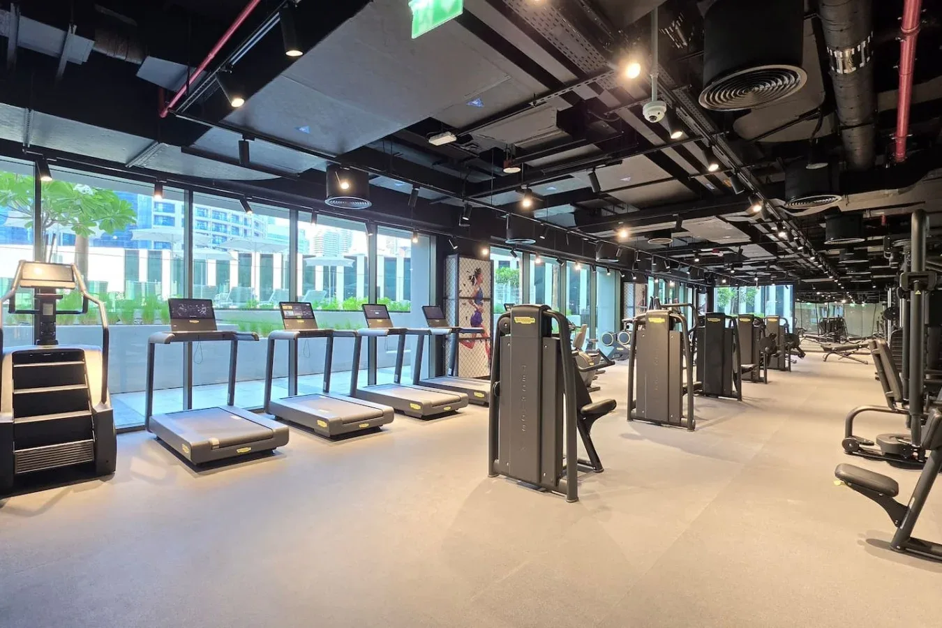 Un gimnasio con cintas de correr y equipos de ejercicio junto a grandes ventanas.