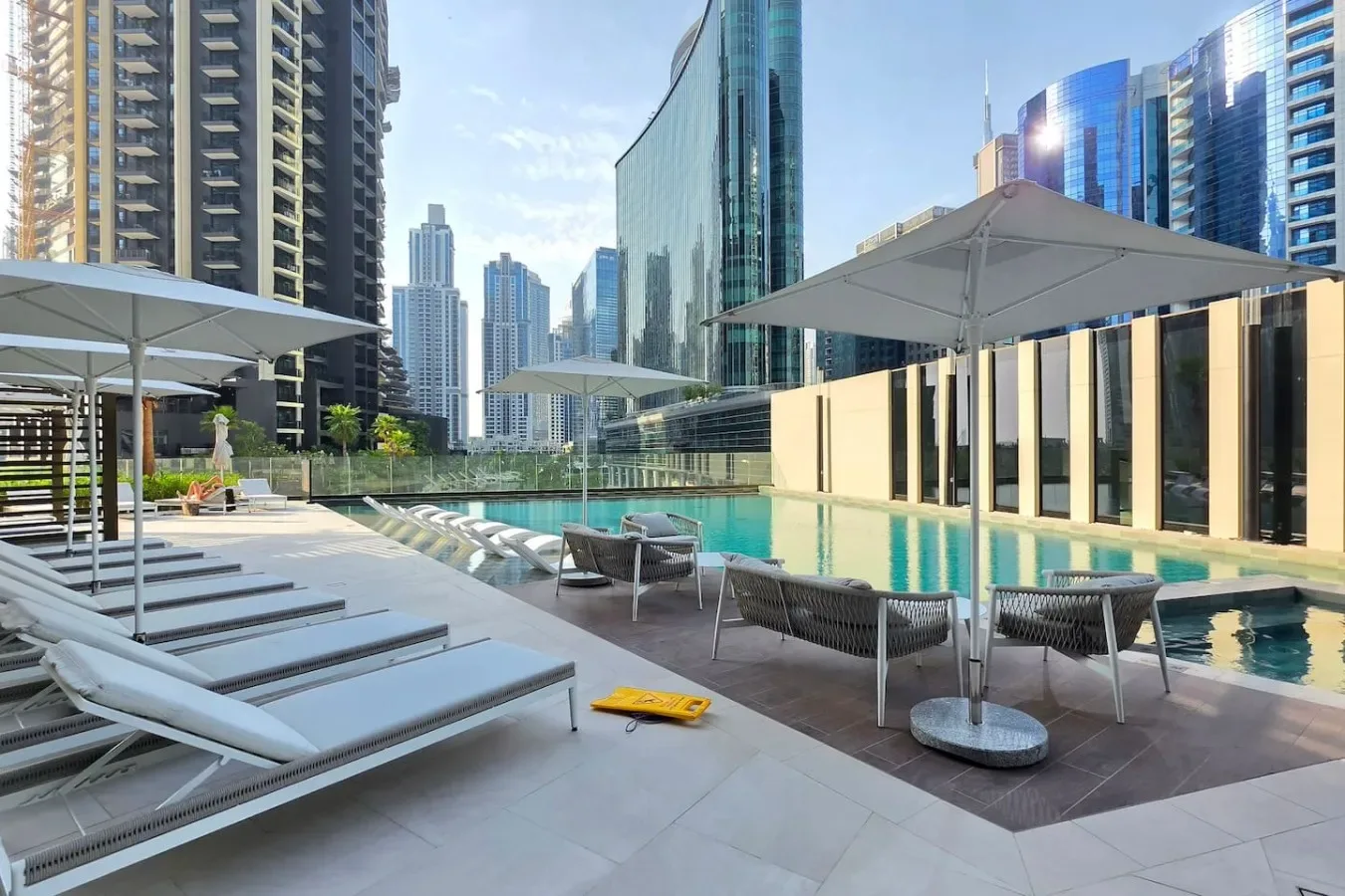 Terraza con piscina, tumbonas, sombrillas y edificios altos de la ciudad.