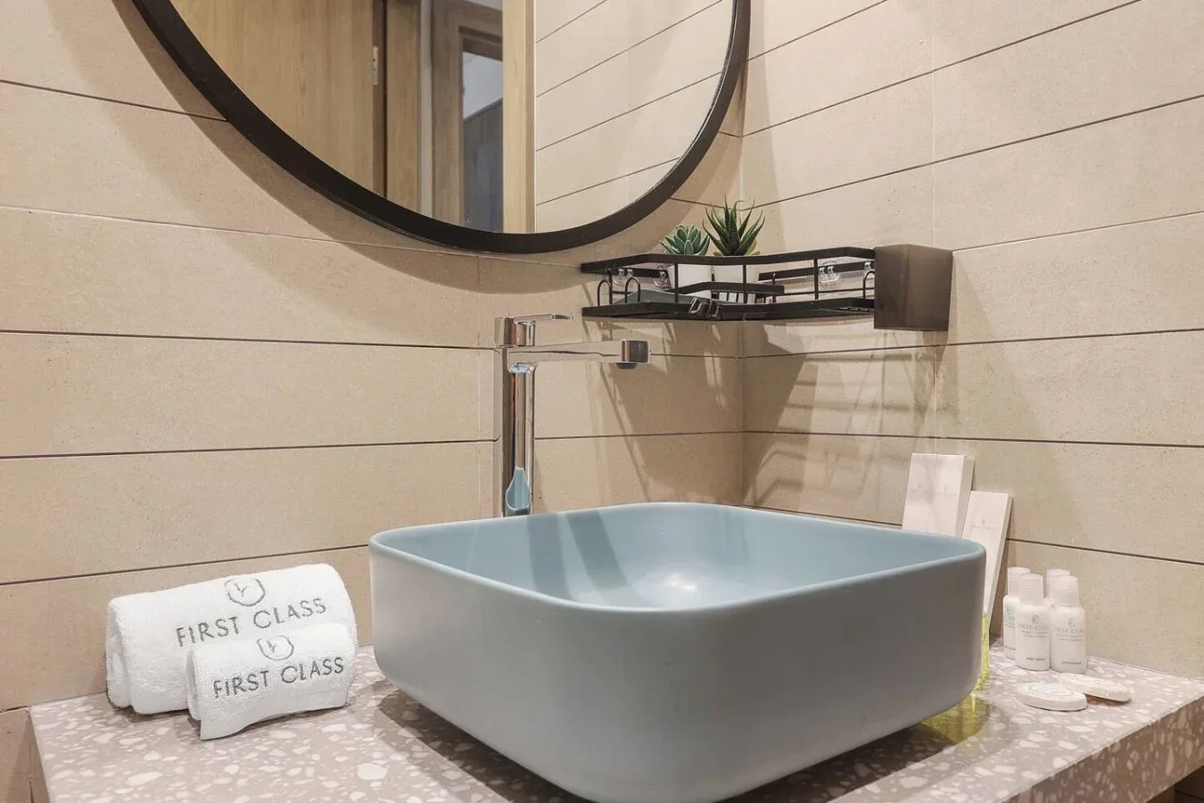 Un tocador de baño cuenta con un lavabo azul claro sobre encimera y un gran espejo redondo.