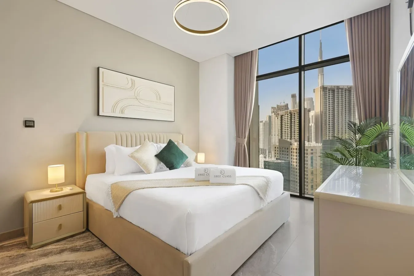 Un dormitorio luminoso con una cama bien tendida junto a grandes ventanales con vistas a edificios de la ciudad.