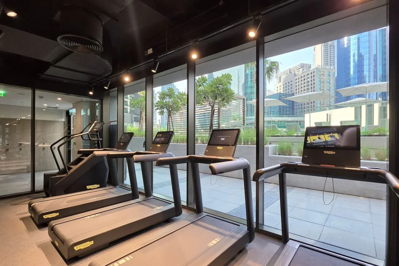 Una sala de ejercicio con cintas de correr junto a grandes ventanales.