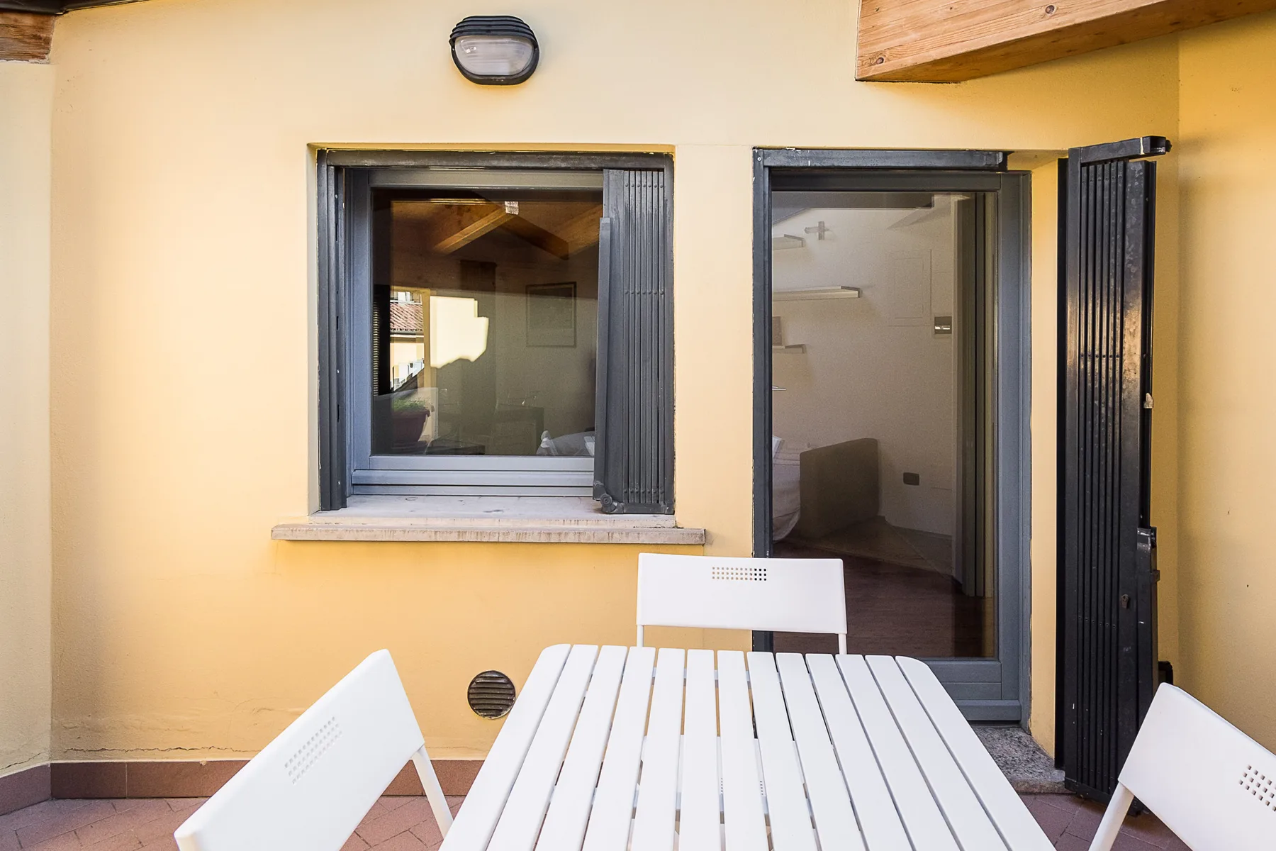 Un comedor al aire libre con una mesa blanca y sillas junto a una pared amarilla.