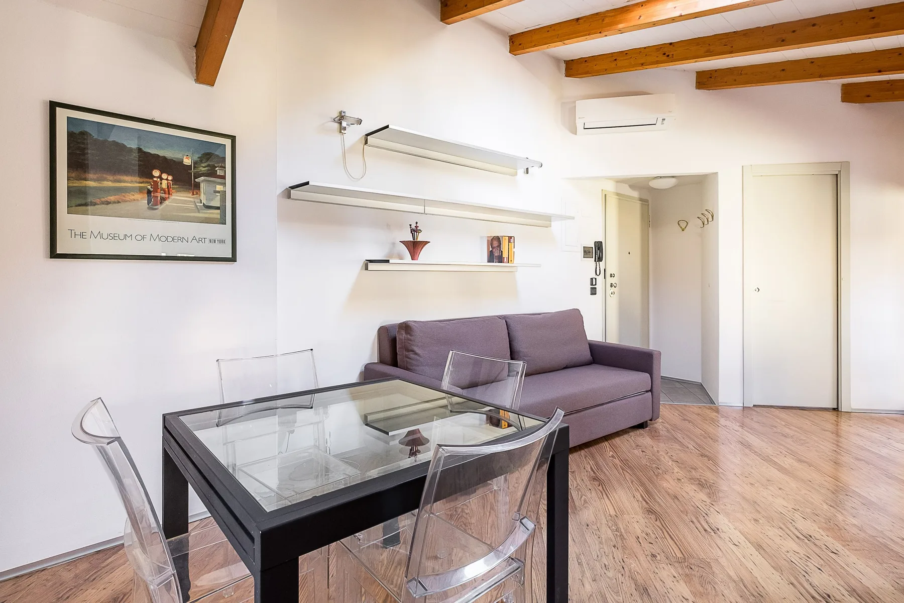 Una sala luminosa con un sofá morado y una mesa de comedor de vidrio.