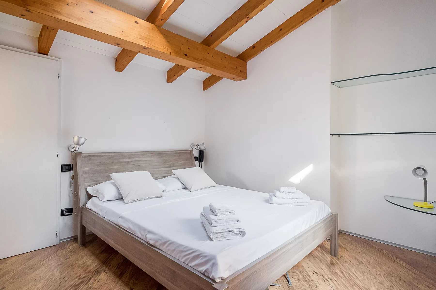 Un dormitorio con una cama doble bajo vigas de madera expuestas.