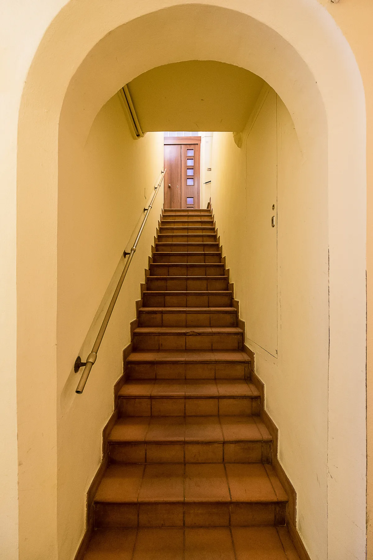 Una escalera interior estrecha sube por un pasaje arqueado hacia una puerta.