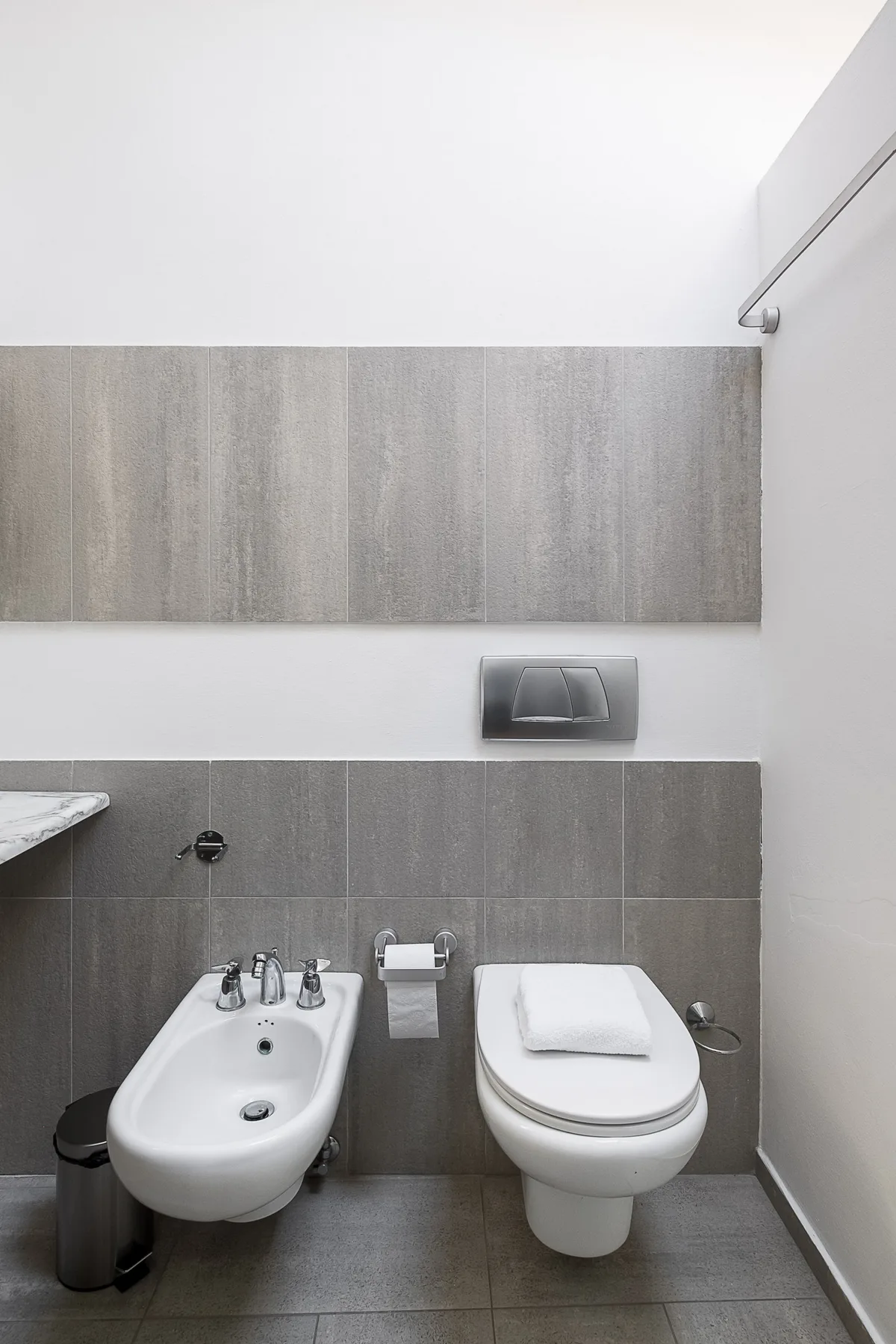 Un baño alicatado con bidé e inodoro bajo una placa de descarga en la pared.