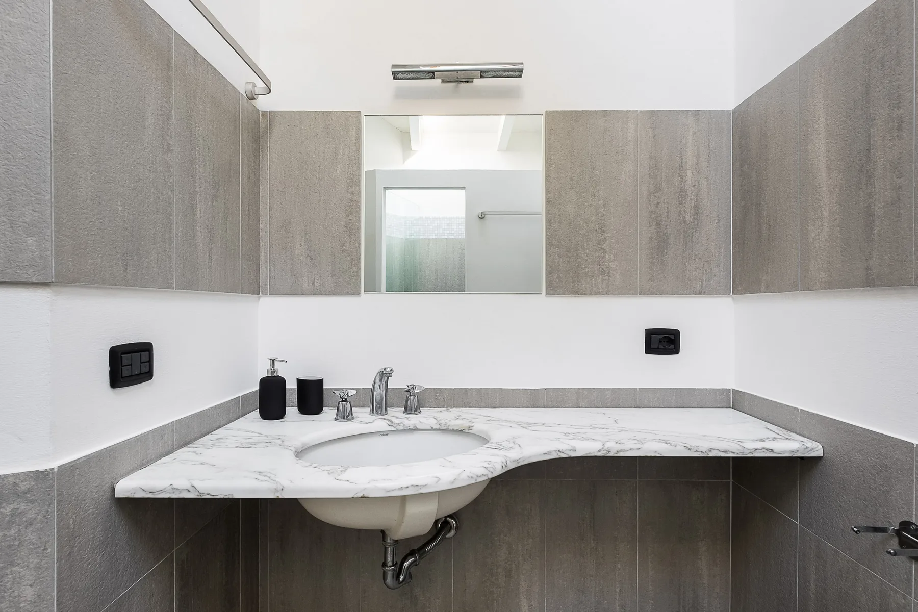 Lavabo de baño con encimera de aspecto marmolado, fregadero y un espejo grande.