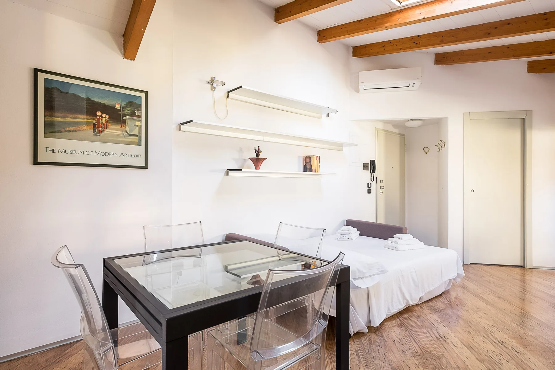 Un dormitorio con una cama junto a una mesa de vidrio y sillas.