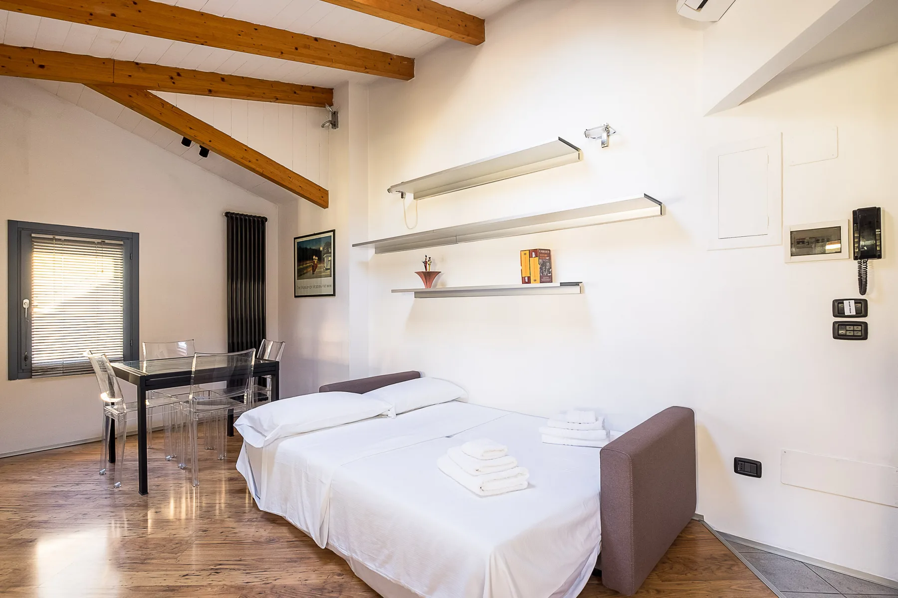 Un dormitorio luminoso con una cama bien hecha y una pequeña mesa de comedor.