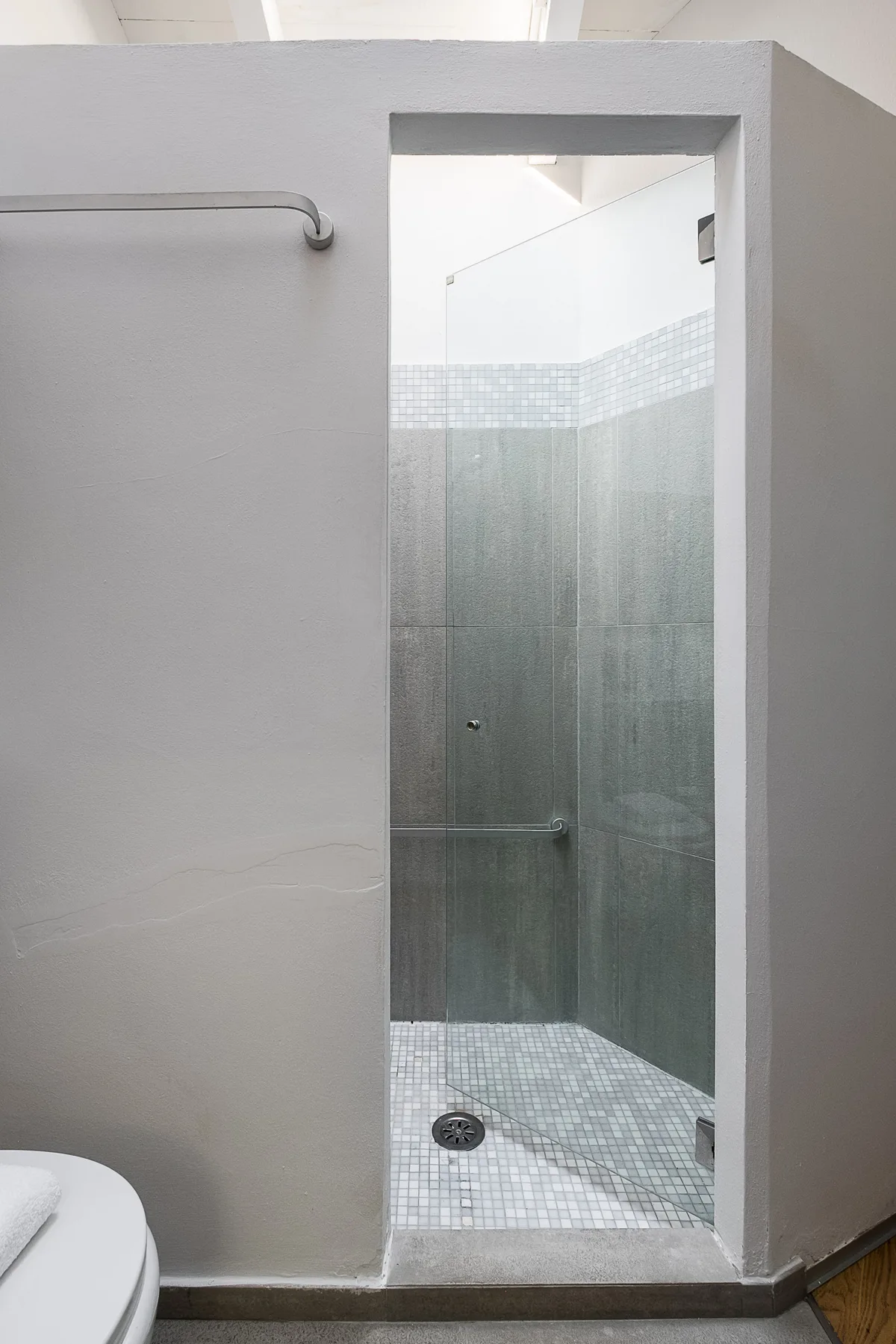 Una ducha de baño con paredes grises de azulejos y un suelo de mosaico.