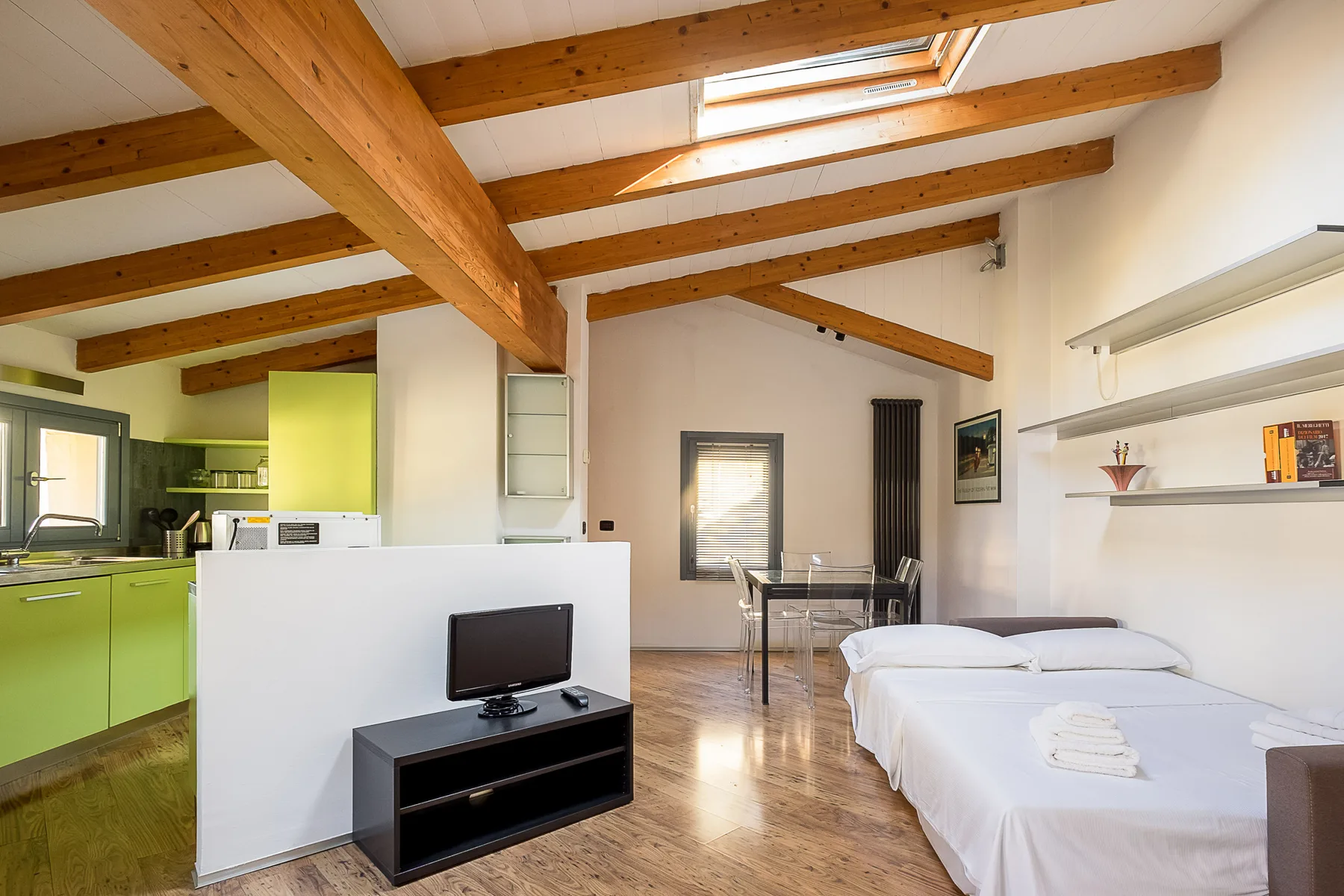 Una luminosa estancia diáfana con armarios de cocina verdes, una mesa de comedor y camas bajo vigas de madera.
