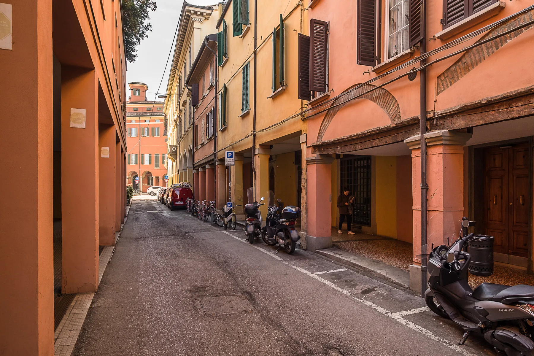 Una calle estrecha bordeada de edificios de tonos cálidos y scooters estacionados.