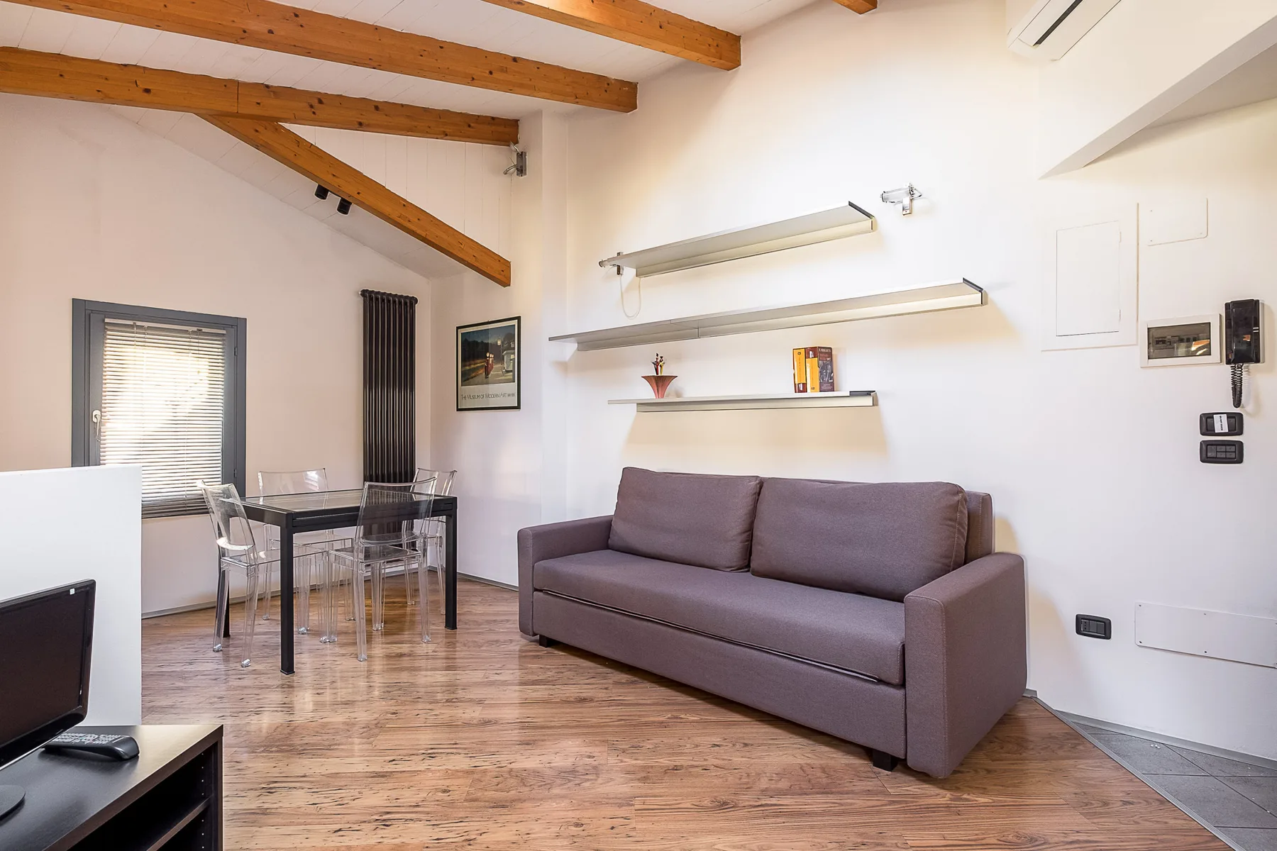 Una sala de estar con sofá, mesa de comedor y vigas de madera expuestas en el techo.